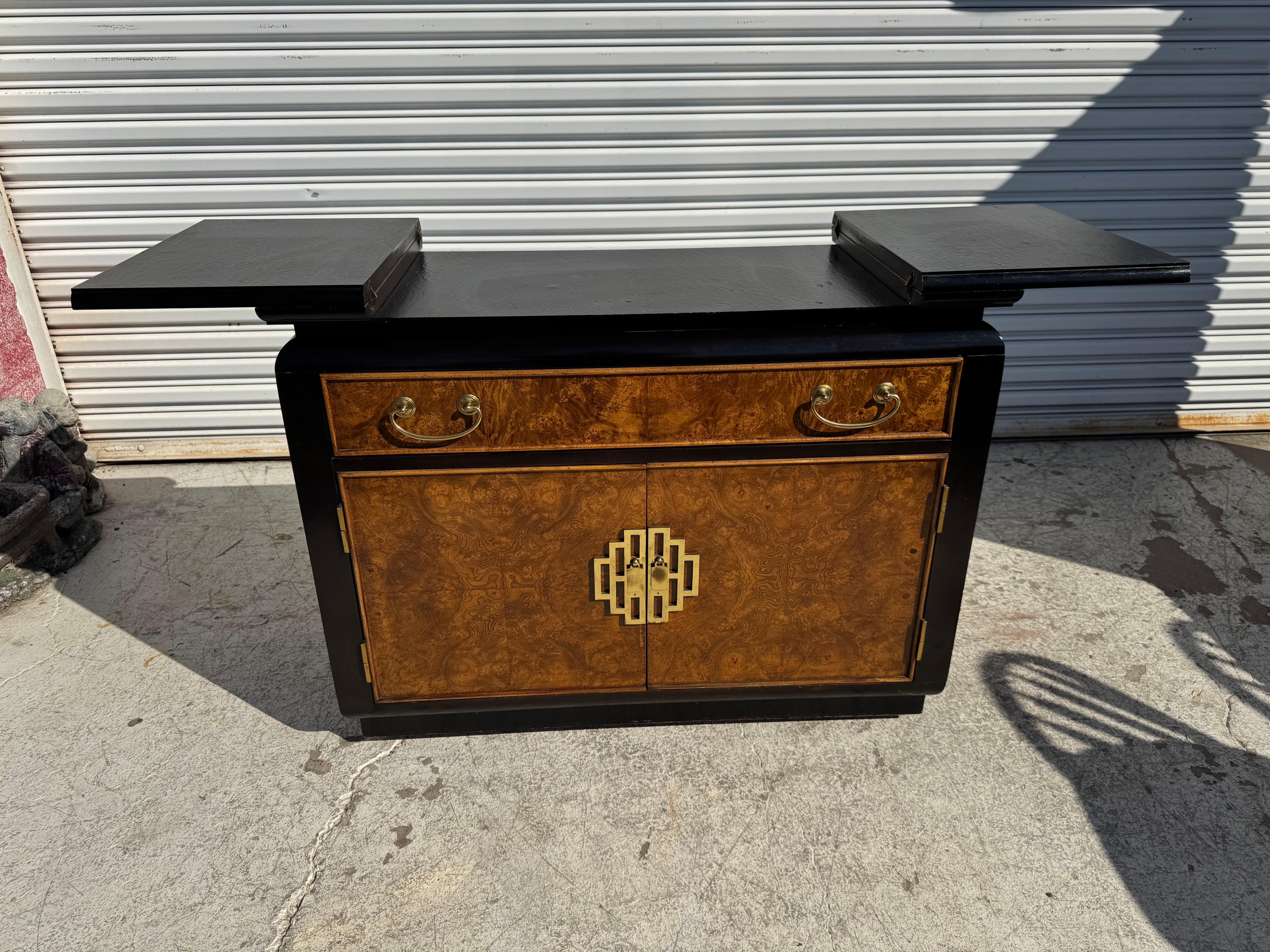 Se trata de un servidor muy bien fabricado por la empresa Century Furniture.
El servidor está hecho en estilo chinoiserie.
Es de nogal burl con detalles lacados ebonizados.
Tiene un n cajón superior y dos puertas inferiores para disponer de mucho