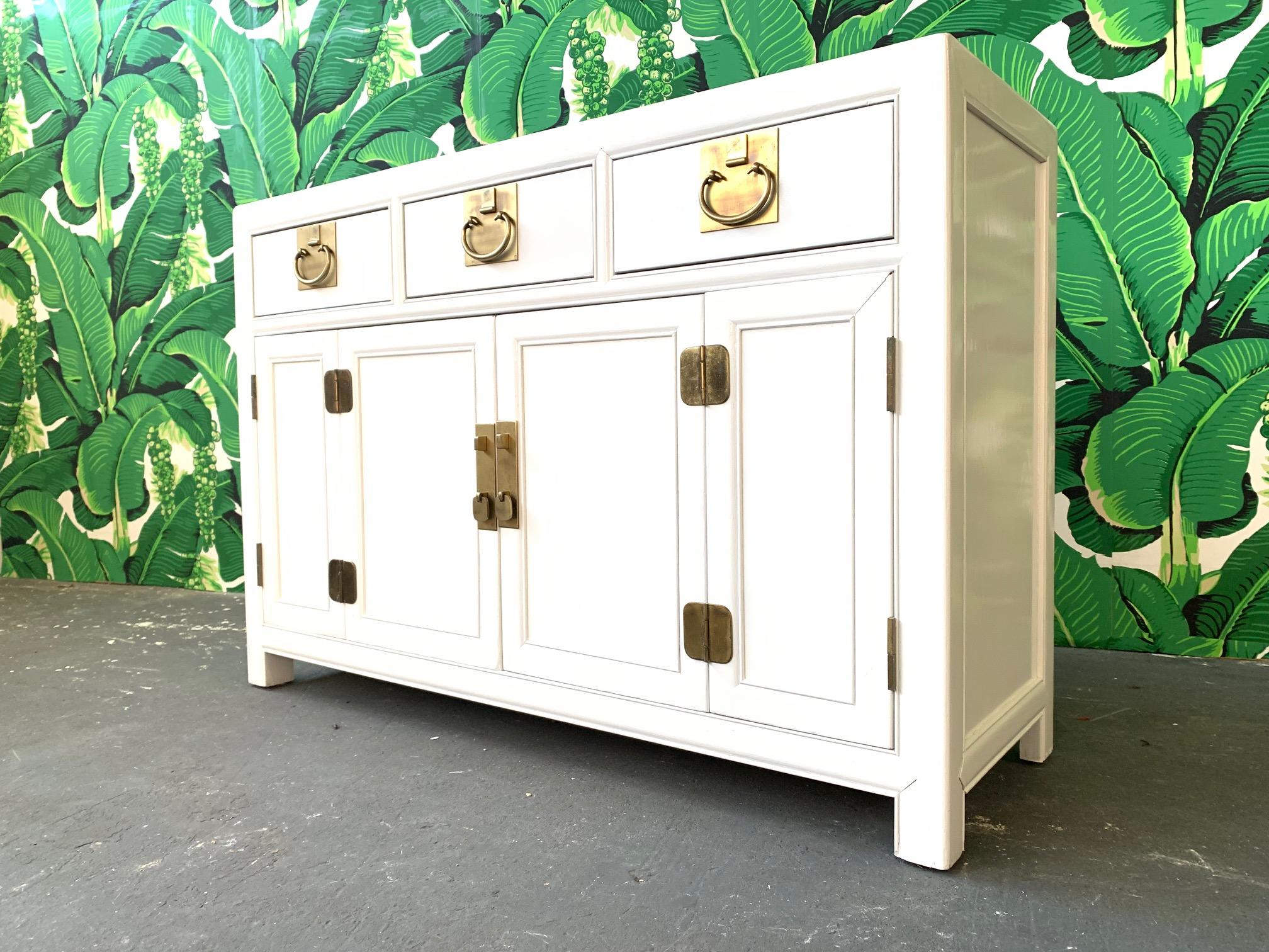 Ming style and brass hardware compliment the white lacquered hardwood of this sideboard made by Century Furniture as part of their Sabota collection. Articulated doors reveal storage cabinet with shelving. Good condition with minor imperfections to