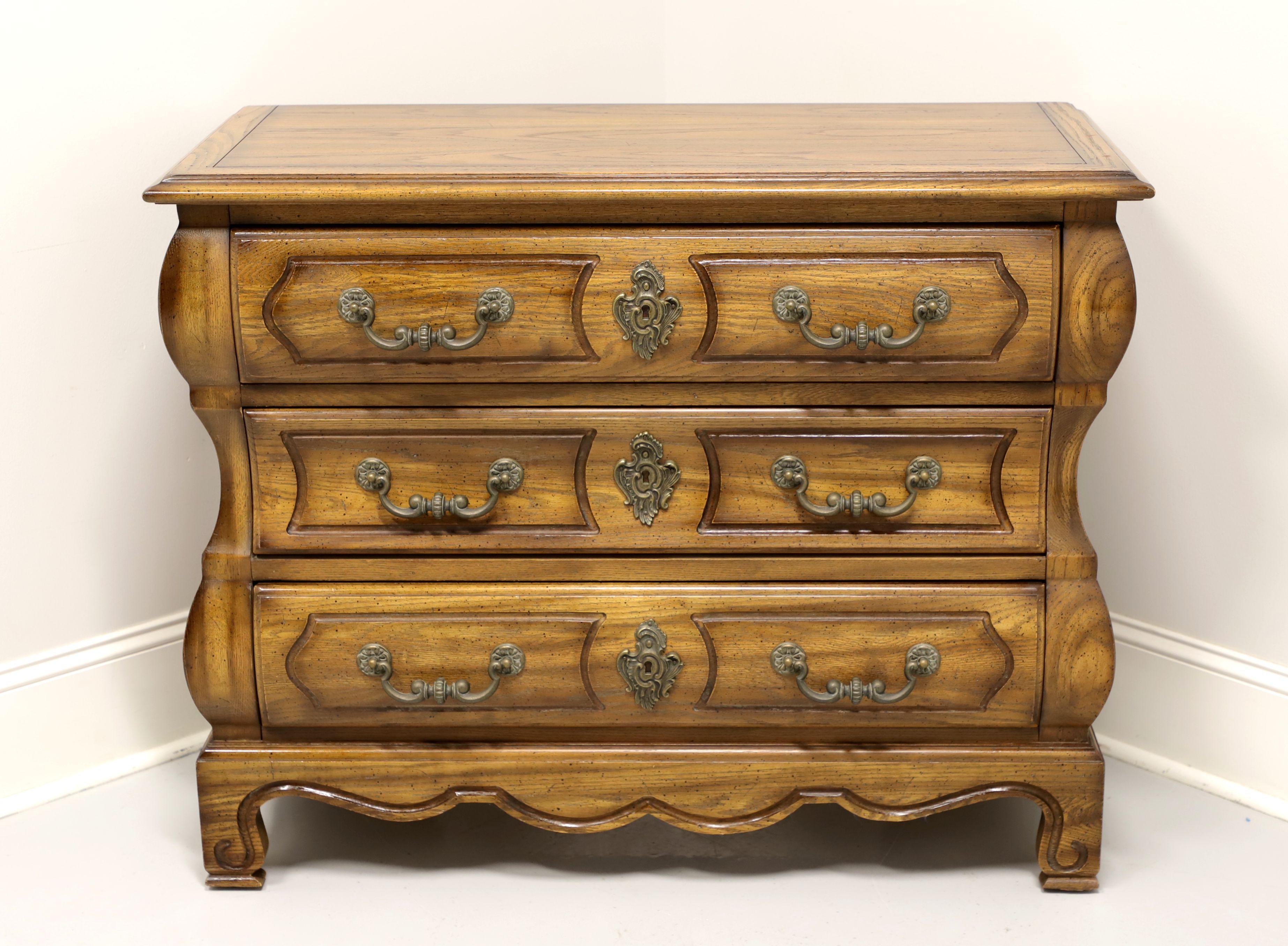 A French Country style bombe bachelor chest, by Century Furniture. Solid oak, brass hardware, bombe style, carved apron and feet. Features three drawers of dovetail construction with faux keyhole escutcheons. Made in the USA, in the late 20th