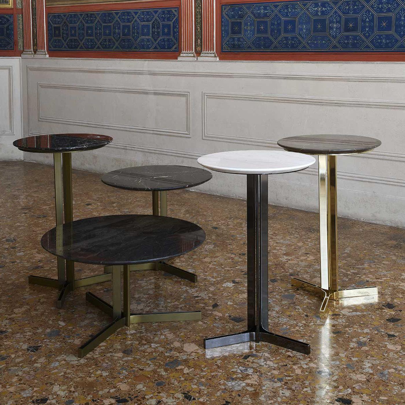 Subtle profiles characterize the restrained aesthetic of this elegant coffee table, inspired by the Titan Ceo that in Greek mythology symbolized wisdom. The metal base, varnished to achieve a burnished brass effect, comprises three elements