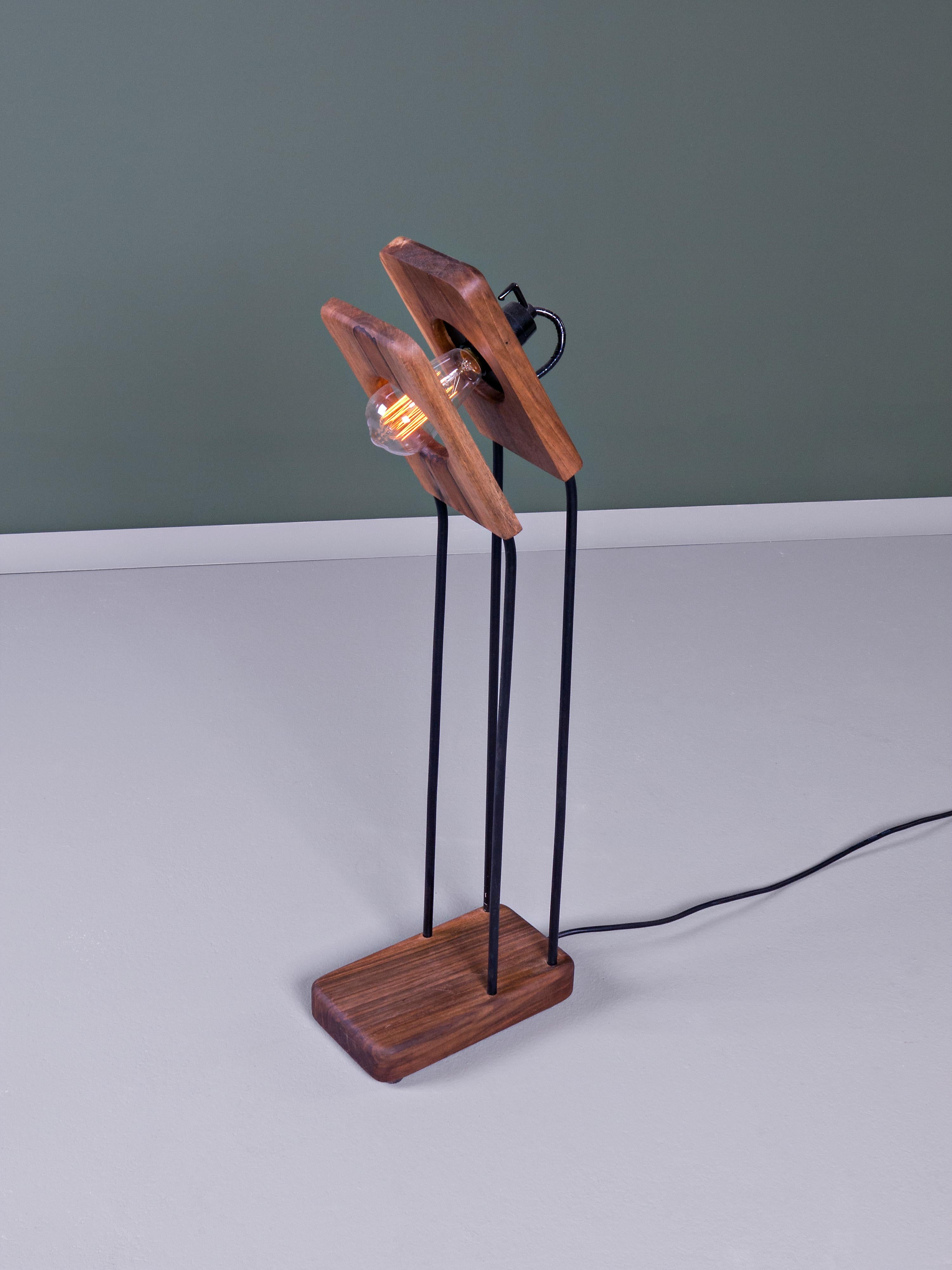 Cette lampe de table est combinée avec du bois et de l'acier. L'intensité spacieuse de cette lampe se compose de deux panneaux de bois d'épaisseur variable séparés par une couche d'air traversée par une source lumineuse, qui sont fixés aux minces