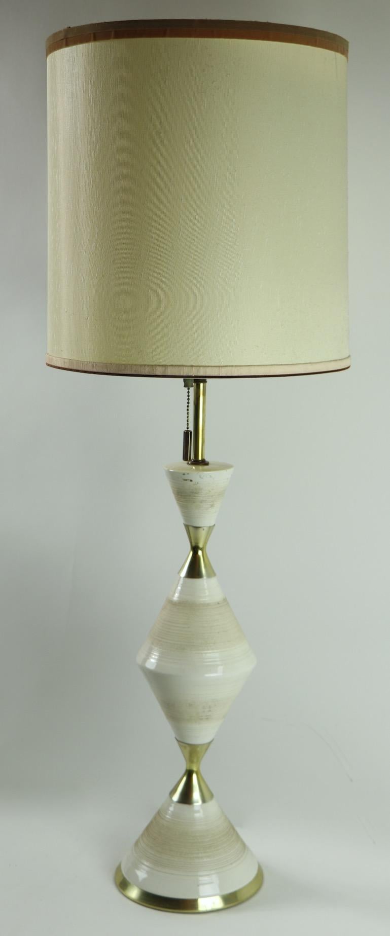 Classic midcentury table lamp, designed by Gerald Thurston. The lamp has a ceramic and brass body of wasted or hourglass, form elements, it is in very fine original, and working condition. The lamp accepts three standard size screw in bulbs, and has