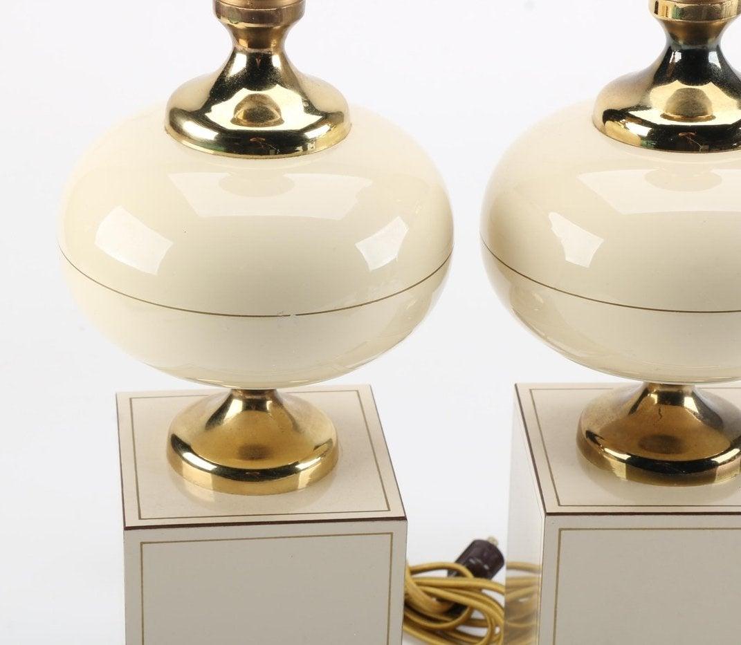 A pair of vintage table lamps with brass accents. 

This selection includes a matching pair of table lamps with gold toned sockets and a curvaceous brass neck, font CAP, and rectangular base.

The bipartite body of each is comprised of an ovoid