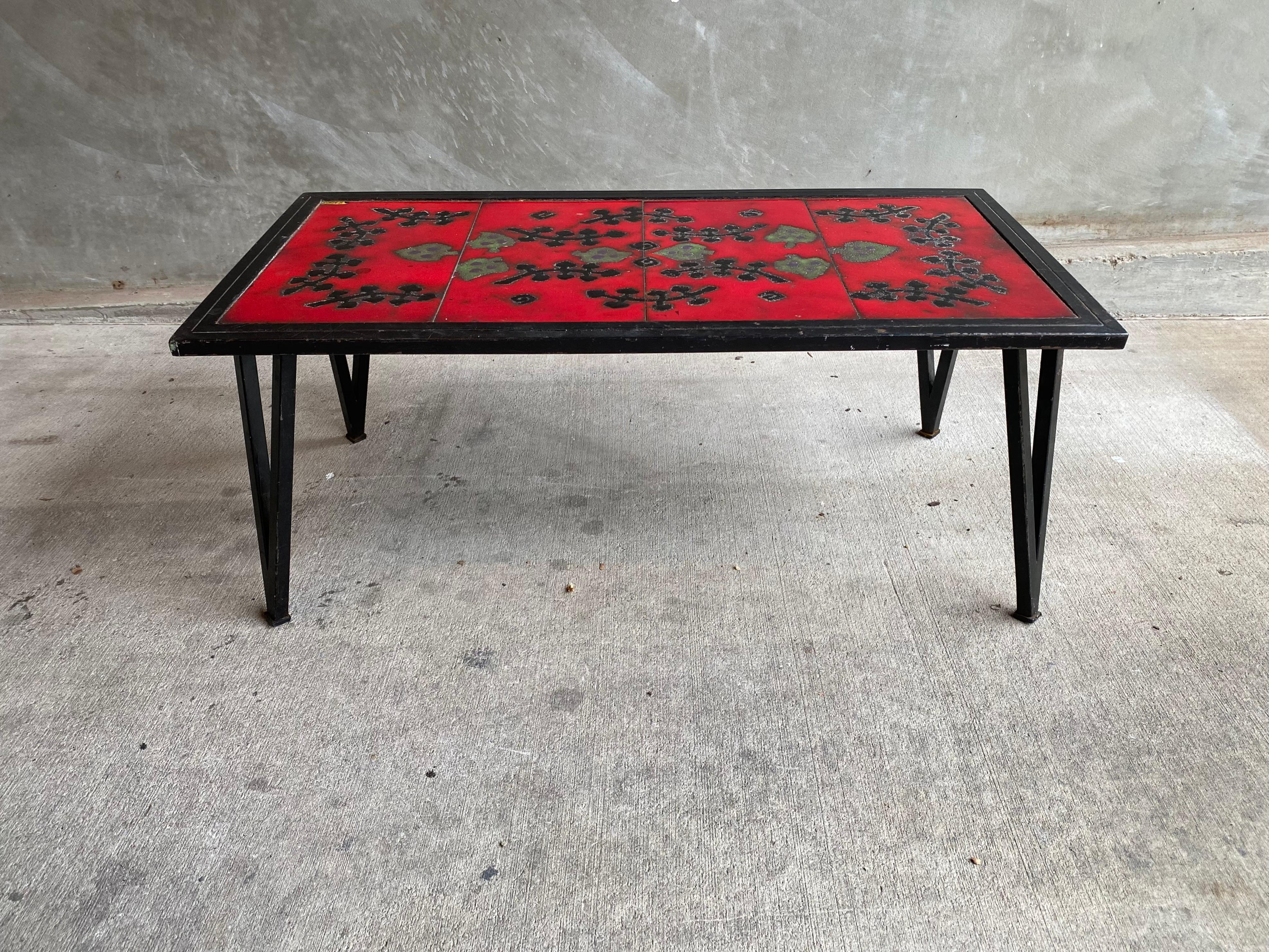 Mid-century glazed ceramic top cocktail table in the style of the French design partners Jacques Adnet and Guidette Carbonell. Steel frame supports 4-piece lava-style tile scene in red and black. France, 1950's.