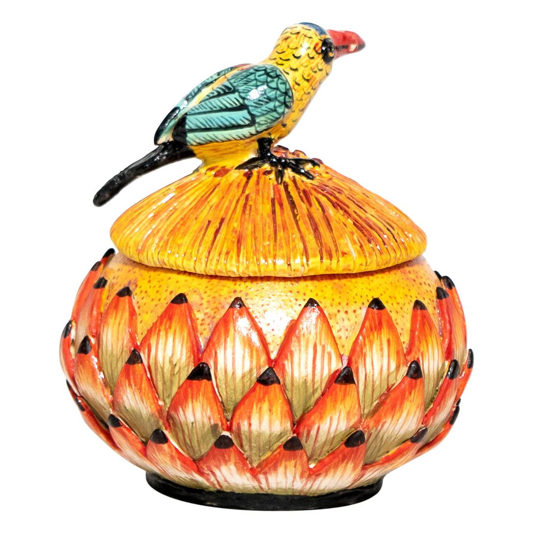 Crafted by Wiseman Ceramics in South Africa, this ceramic Caribbean bird jewelry box measures 5 inches high, 5 inches in length, and 5 inches wide. Hand-sculpted by Thabo and intricately hand-painted by Riya, it reflects a vibrant representation of