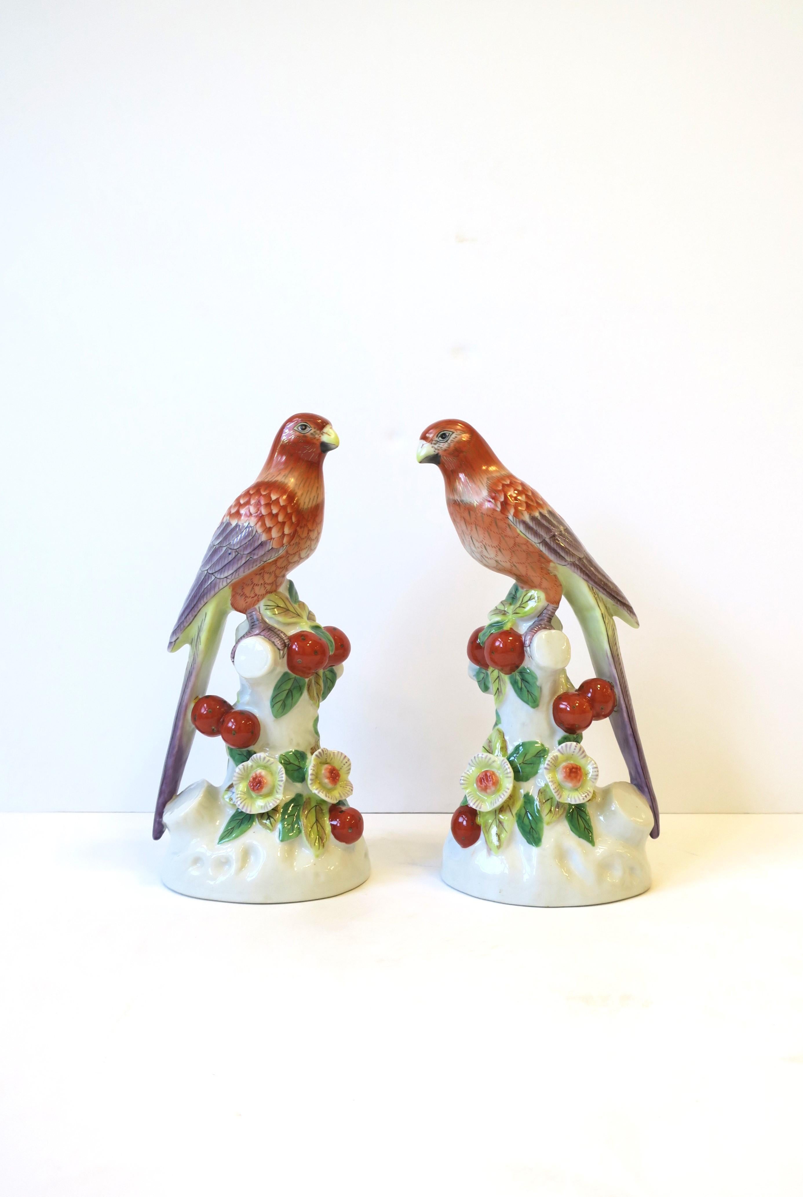 A pair of ceramic bird's decorative objects perched on branch, circa late-20th century. Beautiful birds with long tails, perched on branch, with flowers and berries. Colors include orange, purple, gold, light green, green, and red. Each bird is
