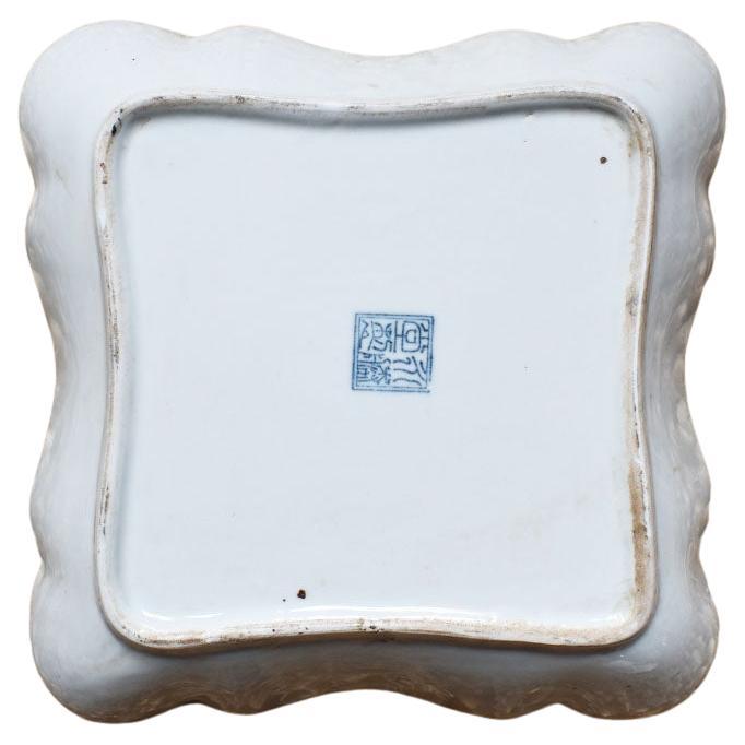 A square ceramic decorative bowl or dish glazed in a blue floral chinoiserie pattern. This vessel would make a great fruit bowl, vide poche, or trinket dish. The sides are scalloped and outlined in a deep dark blue. The center of the bowl is