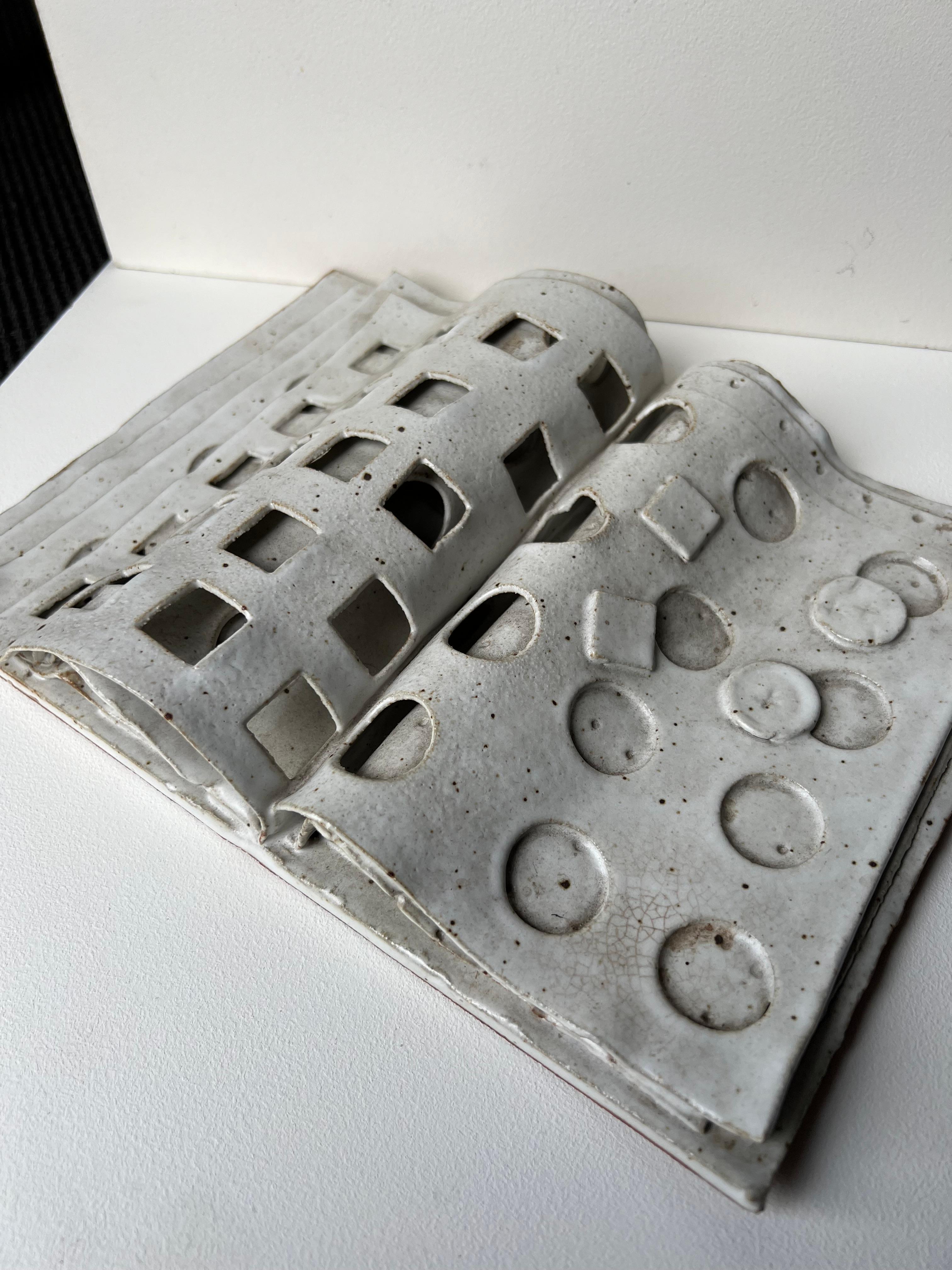 Incredibly unique ceramic artwork by celebrated artist David Korty. Piece is fully ceramic and in the shape/form of a book with multiple square and round cutouts along the pages. Detail of lifted pages also incorporated into the piece to capture