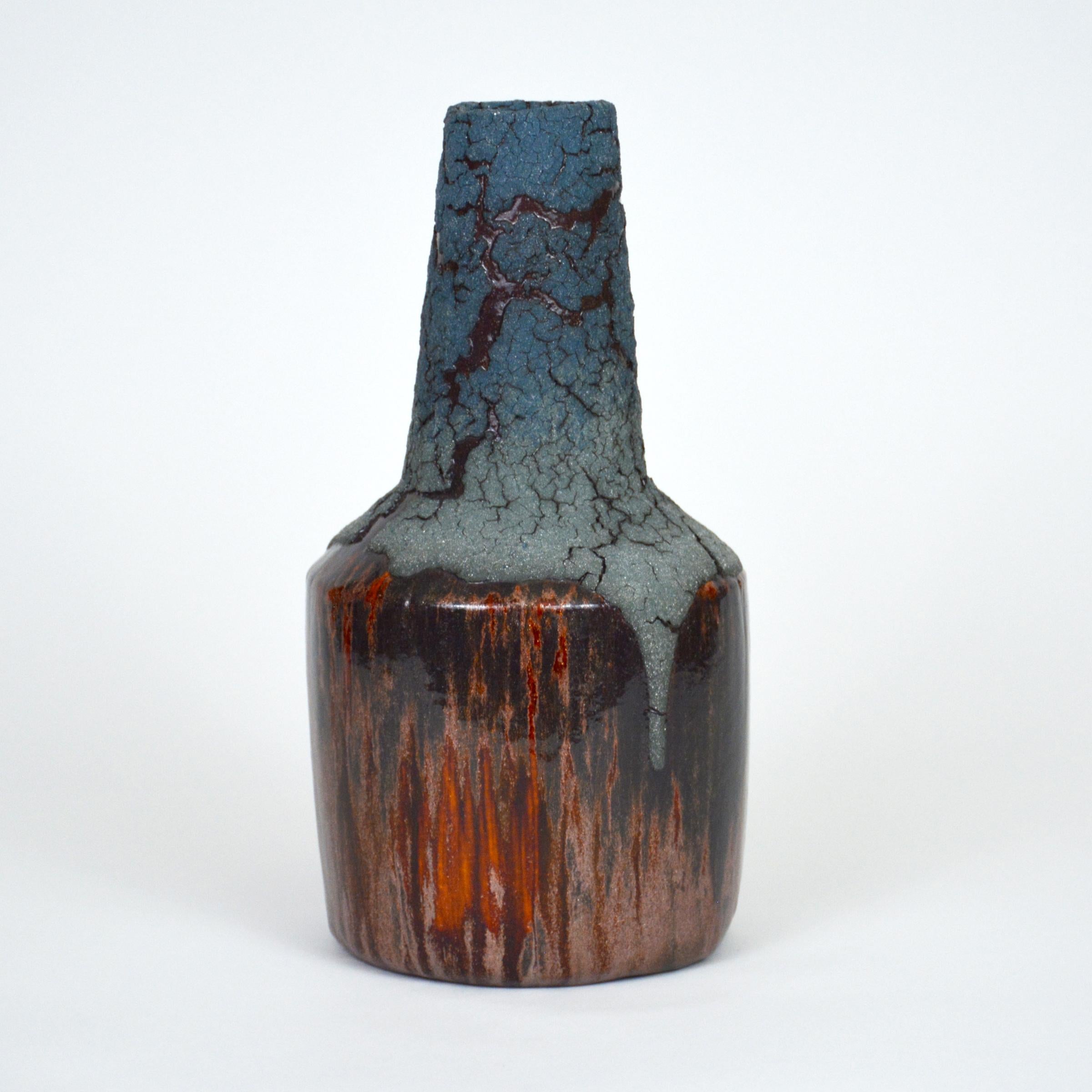 Blue Lava ceramic bottle by William Edwards
Hand built earthenware vessel, fired multiple times to achieve a textured surface of random abstraction, matte blues with shades of amber gloss metallic microcrystalline glaze breaking through that