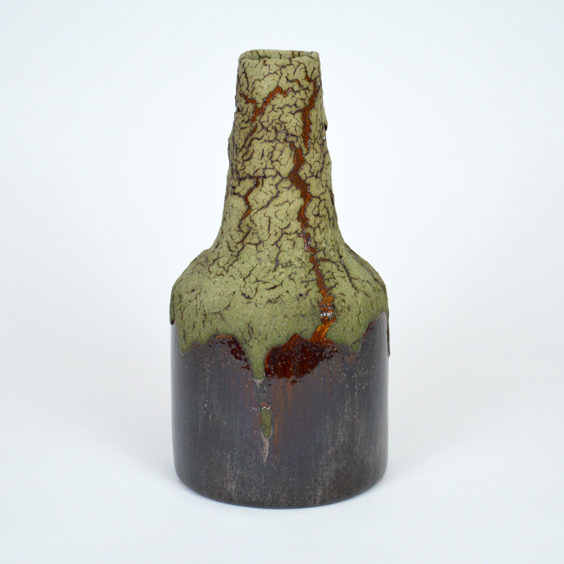Green lava ceramic bottle by William Edwards.
Hand built earthenware vessel, fired multiple times to achieve a textured surface of random abstraction, matte green glaze with dark amber gloss metallic, microcrystalline glaze breaking through that