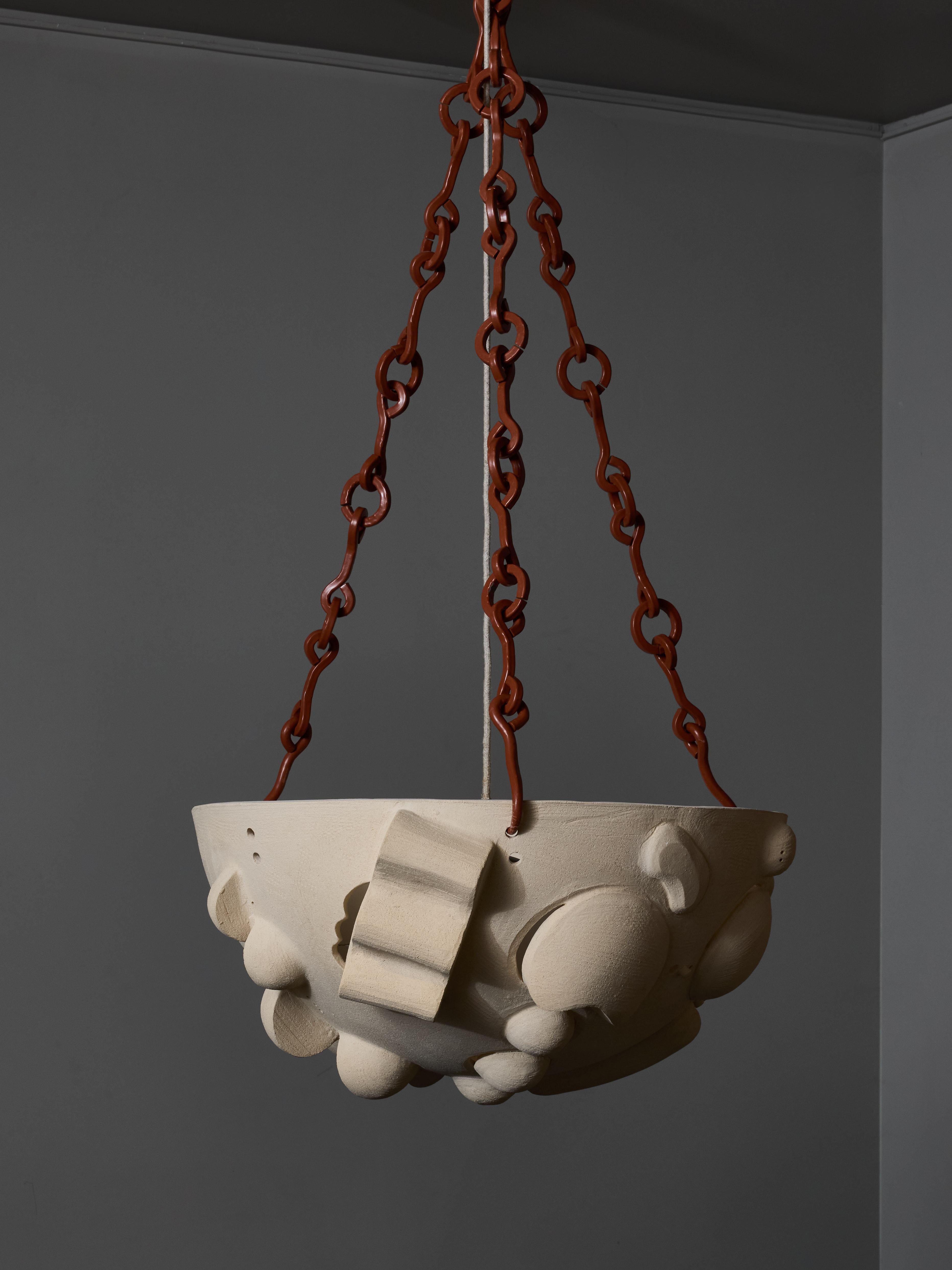 Olivia Cognet reinterpreta la clásica lámpara en forma de cuenco. Esta lámpara de araña está hecha de un cuenco de cerámica grande y profundo, con decoraciones abstractas en relieve y una abertura para dejar pasar la luz, aportada por un cristal