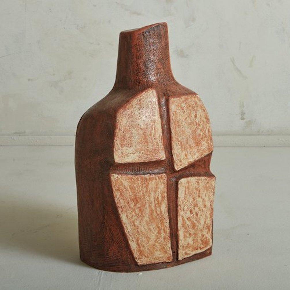 A vintage ceramic sculpture featuring a bottle shape in a rust brown hue with a raised cream decorative shapes on the front and back. This piece has great scale and a beautiful textured finish. Signed ‘Lado ‘81’ on base. Sourced in Italy.

