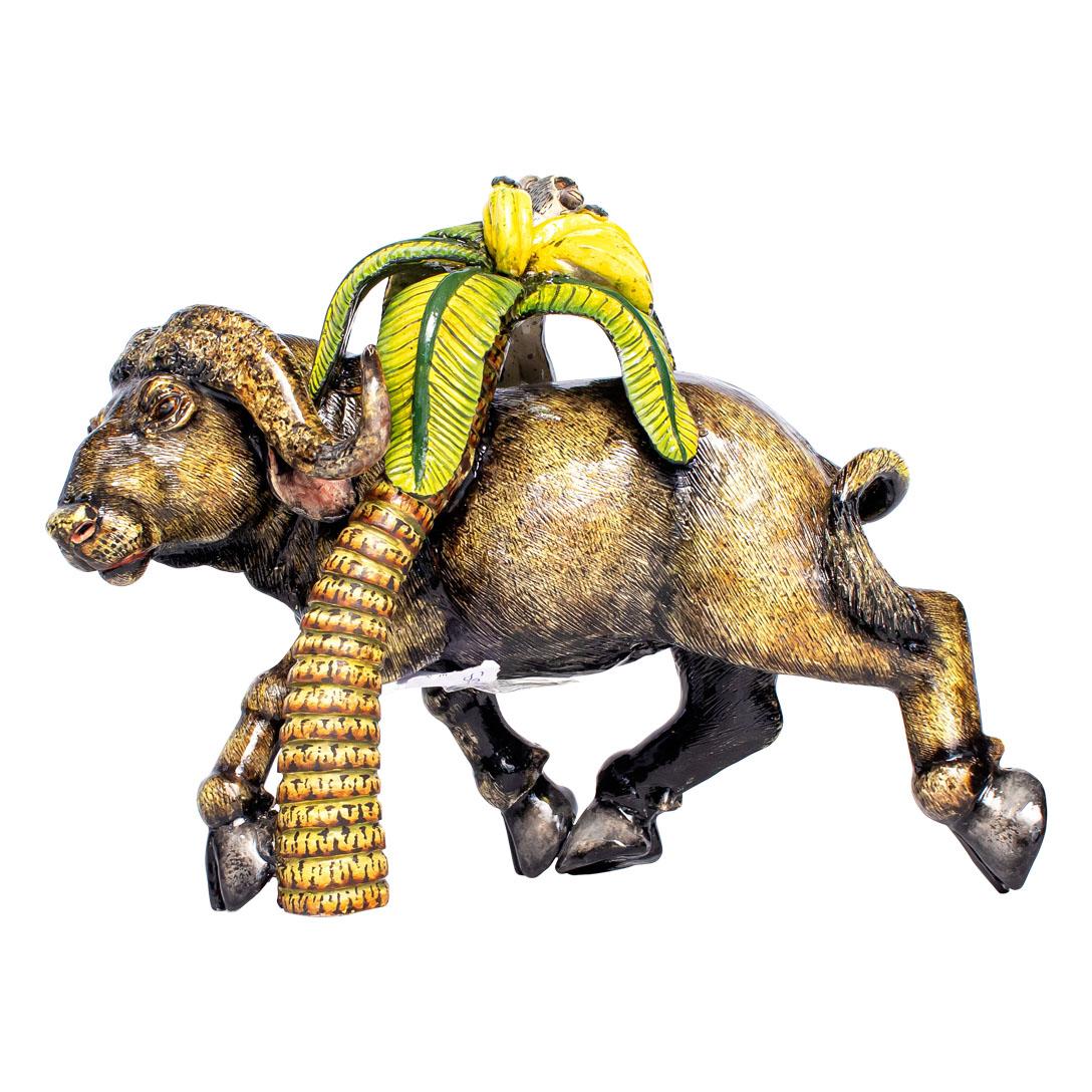 Senzo Duma Ceramics presents a striking ceramic Buffalo & Monkey sculpture, standing 9 inches tall with dimensions of 11 inches in length and 5 inches in width. Hand-painted by Mlu, the sculpture captures the essence of African wildlife, where the