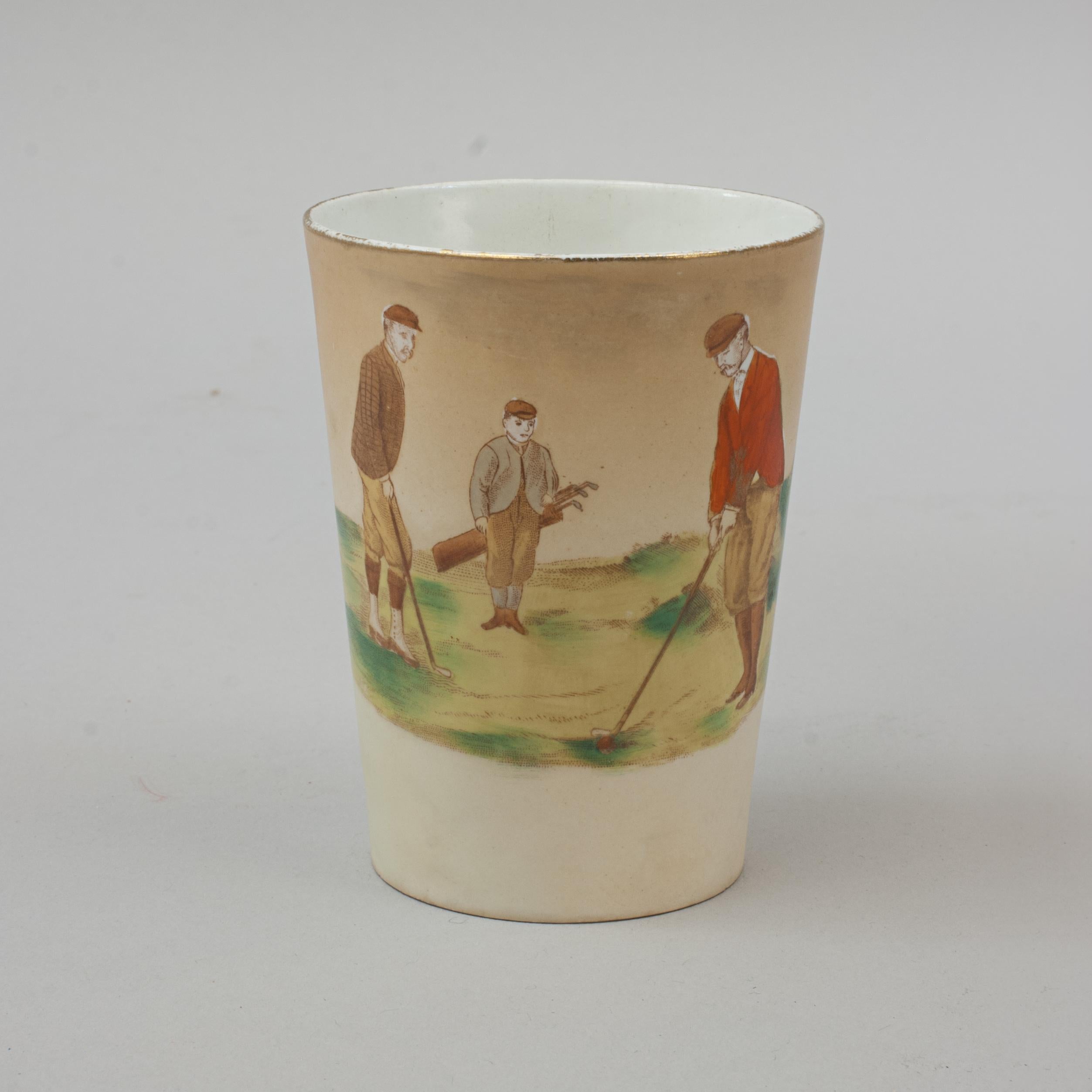 Wiltshaw & Robinson Carlton Ware Golf Beaker.
A ceramic Carlton Ware beaker with a golfing scene and gilt rim. The golf scene shows one golfer dressed in a red coat about to strike the ball watched by another player and a caddy. The bottom on the