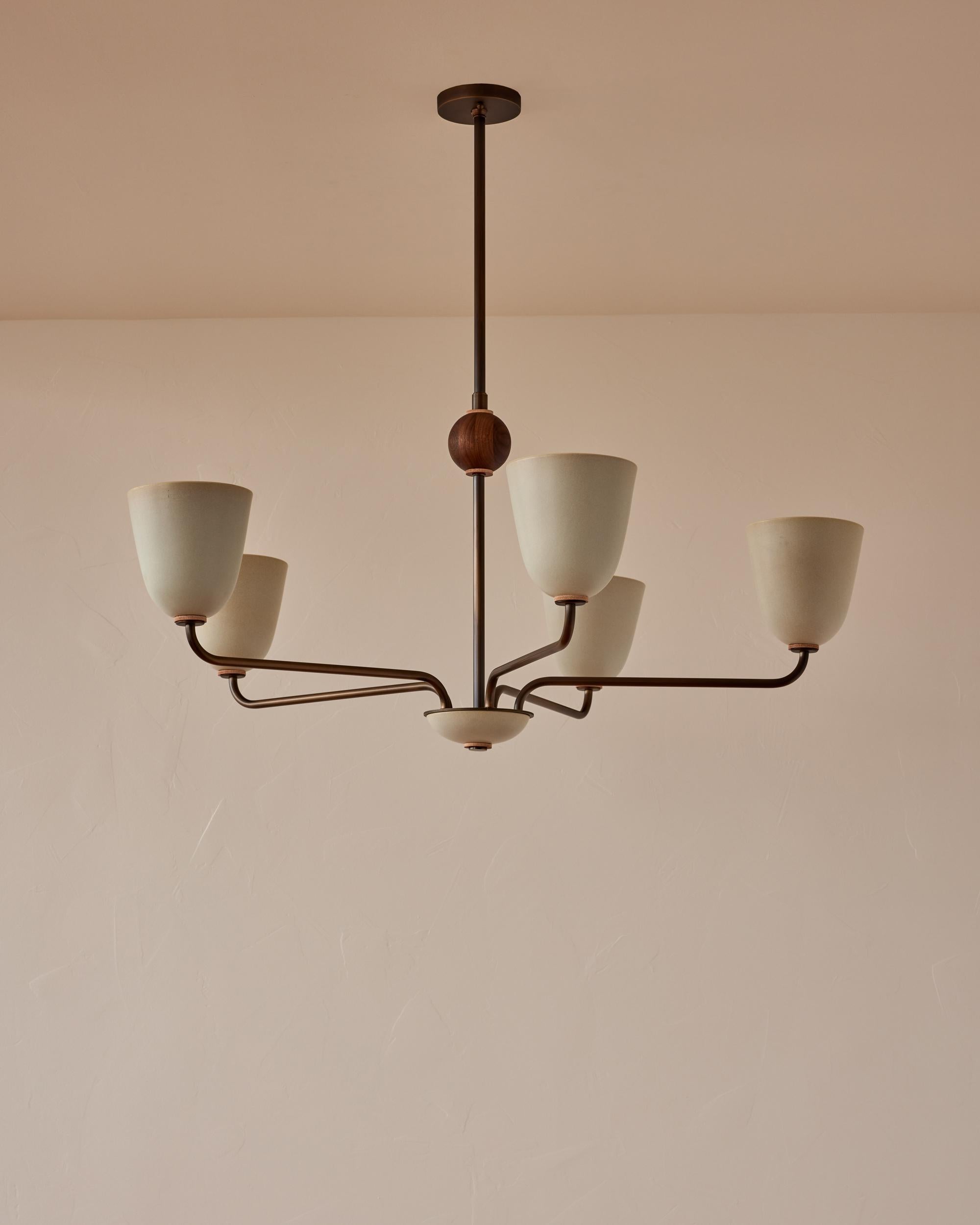 Five antique brass patina arms curve up from a ceramic cluster dish to three tall stoneware ceramic shades in Robin's Egg, a matte glaze with a tinge of blue. With a fixed black walnut orb and tan harness leather accents, this graceful chandelier