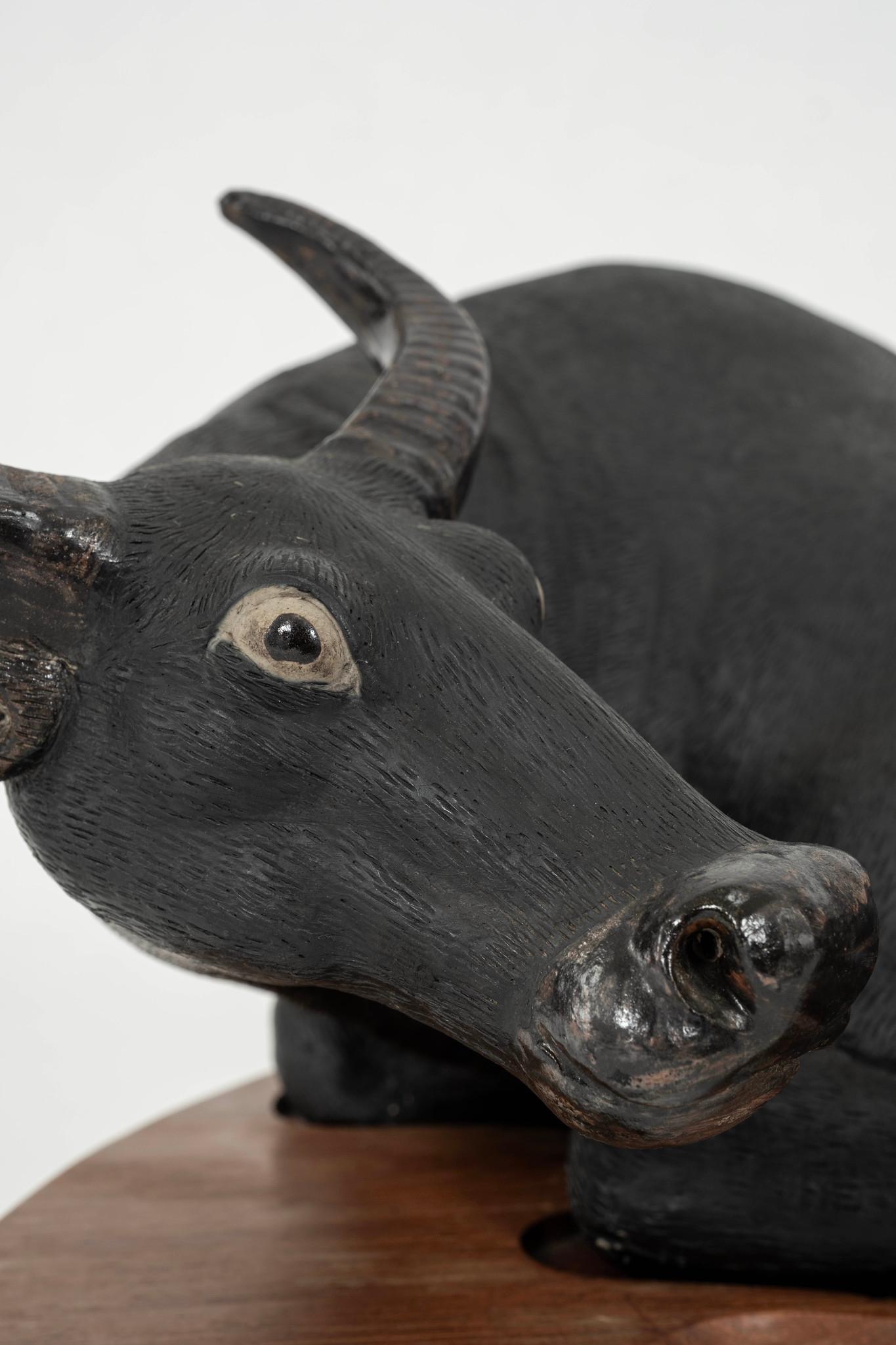 Scultura di bue in ceramica cinese dei primi del Novecento con finitura pettinata e leggermente strutturata, decorata con uno smalto opaco. La scultura supina poggia su una base di legno.

