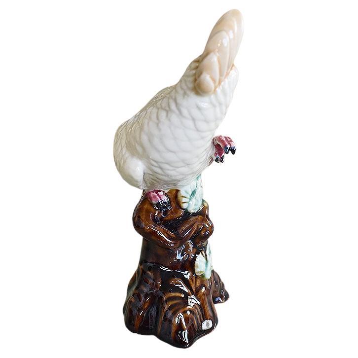 A petite ceramic bird figurine glazed in a creamy white with yellow feathers and pink details. This cockatoo sits upon a brown tree branch with lush green leaves. 

Dimensions:
7.25