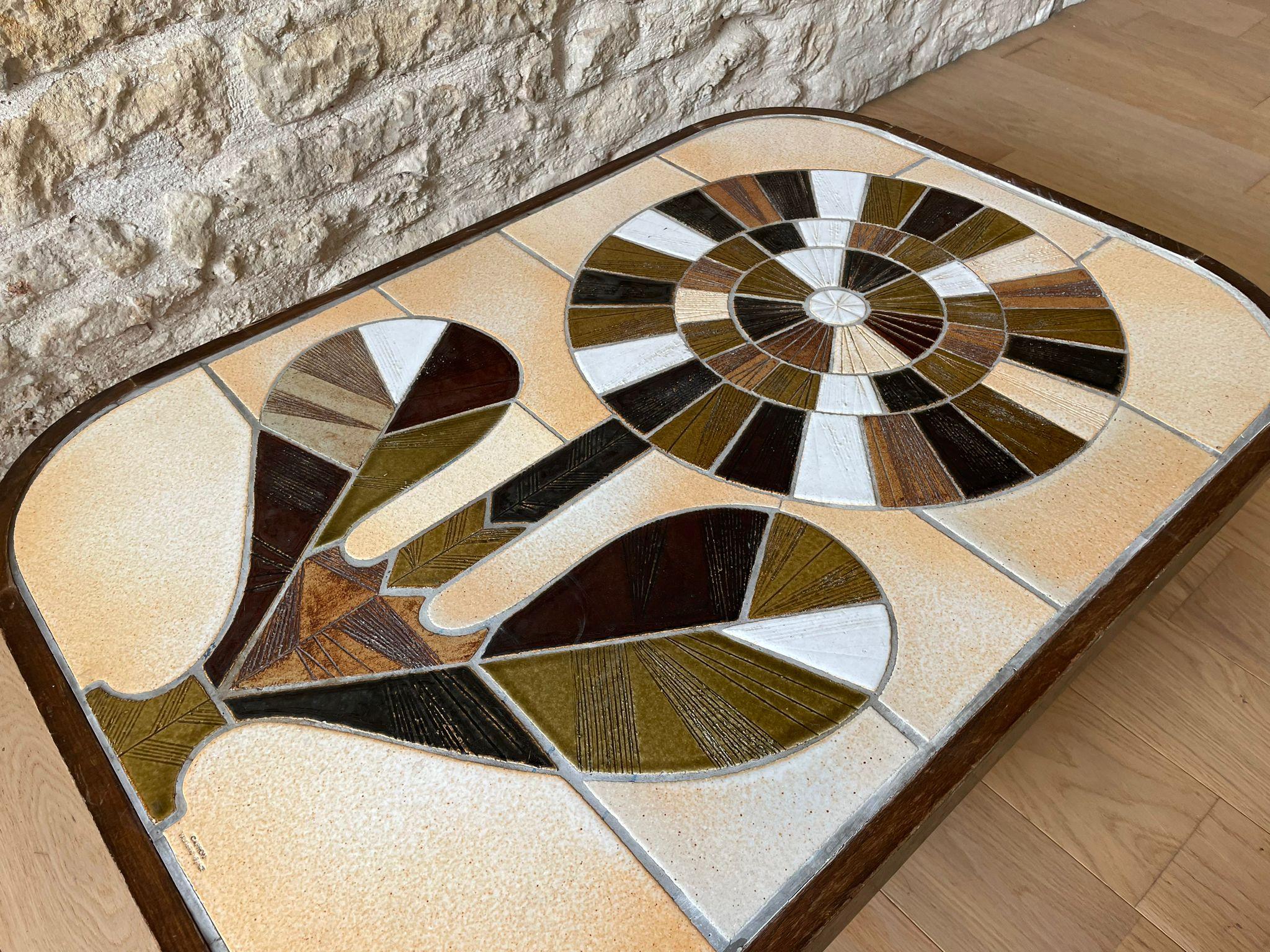 Cette exquise table basse française met en valeur l'art du célèbre céramiste Roger Capron. Le plateau de la table présente un motif floral saisissant composé de carreaux de céramique émaillée disposés de manière complexe dans des tons terreux,