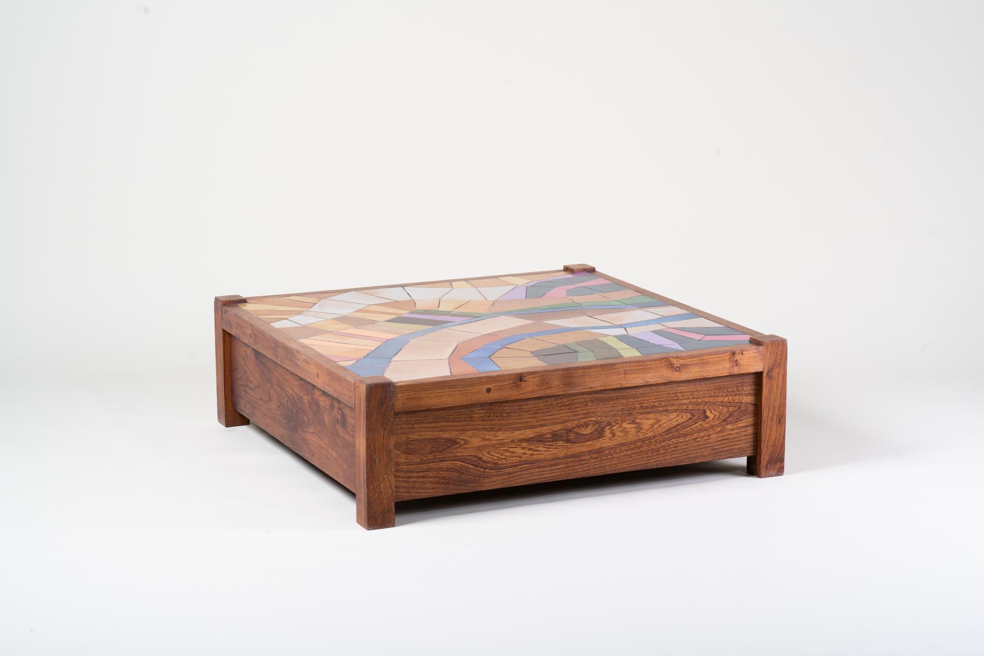 A striking handcrafted coffee table dating from the 1970s, combining the warmth of solid wood with the artistry of a colorful ceramic tile mosaic top. The square form is framed by robust wooden legs and panels, giving the piece a grounded and