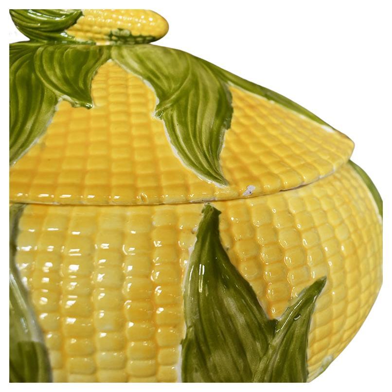 A wide corn motif ceramic serving tureen. Hand-painted in yellows and greens, this lovely dish is wide and oval in shape. Along the sides, textured yellow corn kernels cover the base among green corn husks. A small green leaf serves as a handle on