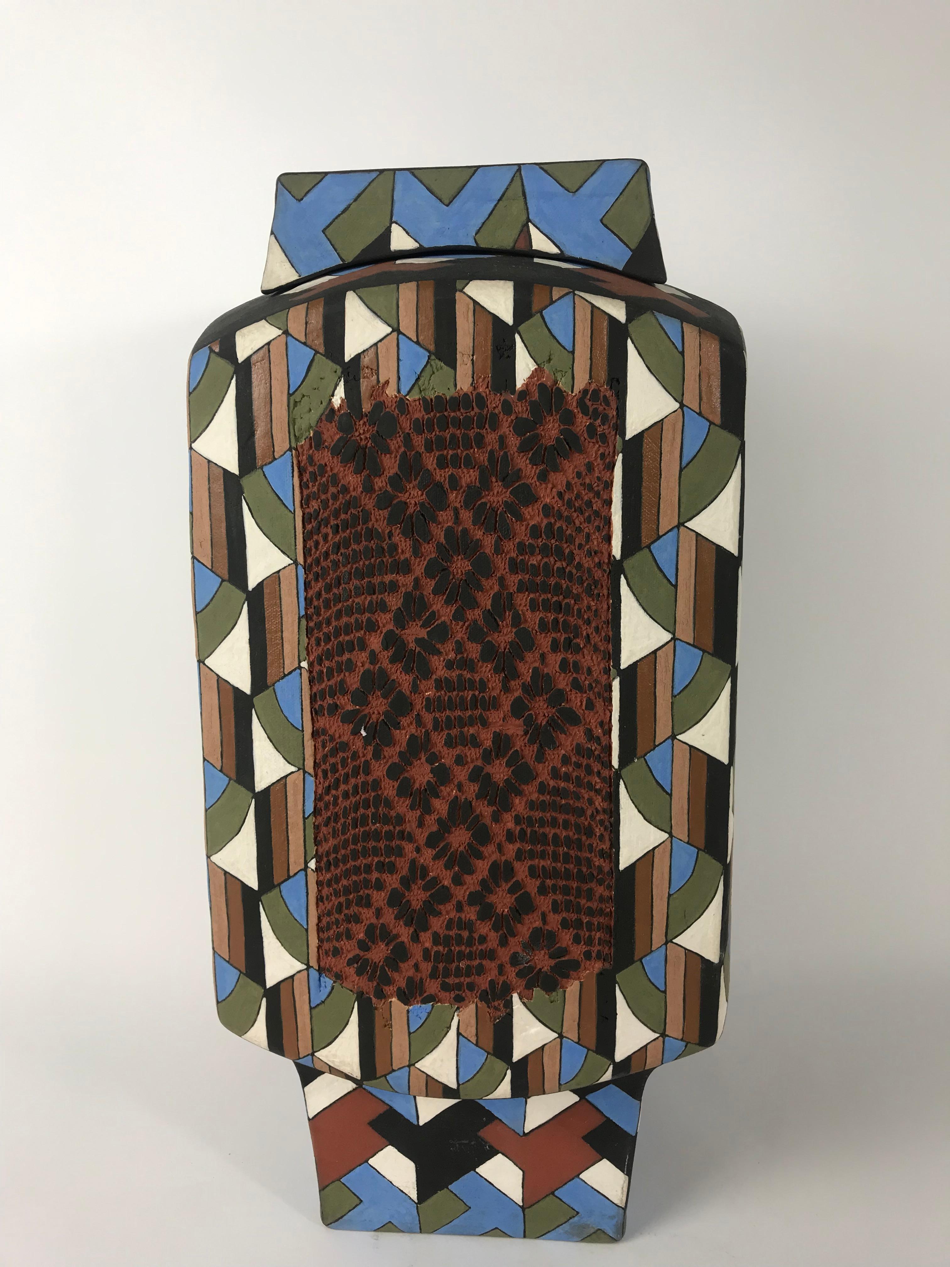 A mind bending abstract covered ceramic vase by Phillip and Marilyn Garnick. This vase features a unique cubic design blended by abstract geometric patterns in a sharp and sleek finish of fair tones of blue, green, black and brown. The final touch