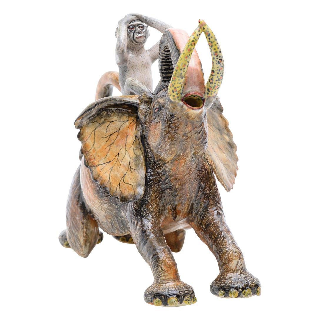 The ceramic Elephant and Monkey teapot from Imvelo Natural Art in South Africa is a captivating piece standing 11 inches high, 13 inches long, and 8 inches wide. Hand-sculpted by Bernard and beautifully hand-painted by artisan Palesa, it features a