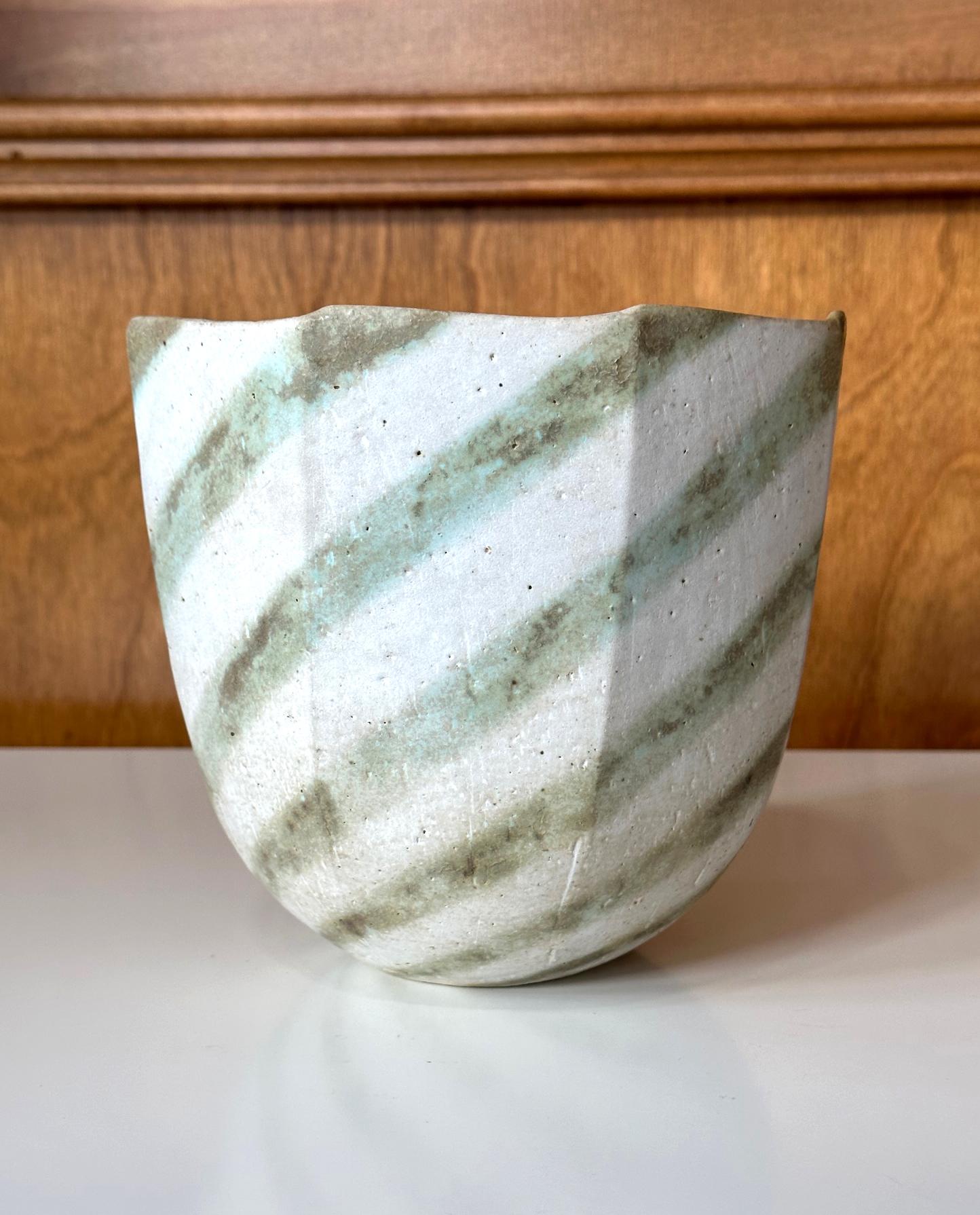 A stoneware vessel with banded stripe glaze made by British studio potter John Ward (1938-2023) circa last quarter of 20th century. The vessel takes an interesting multi-faceted form with a large opening and stands on a small, tapered base. In