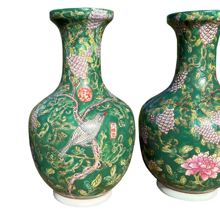 A pair of ceramic famille verte green chinoiserie vases. Glazed in a beautiful deep green, and decorated with a floral motif of pink chrysanthemums, purple berries, birds on branches, and red Chinese characters. This pair will be fabulous on an
