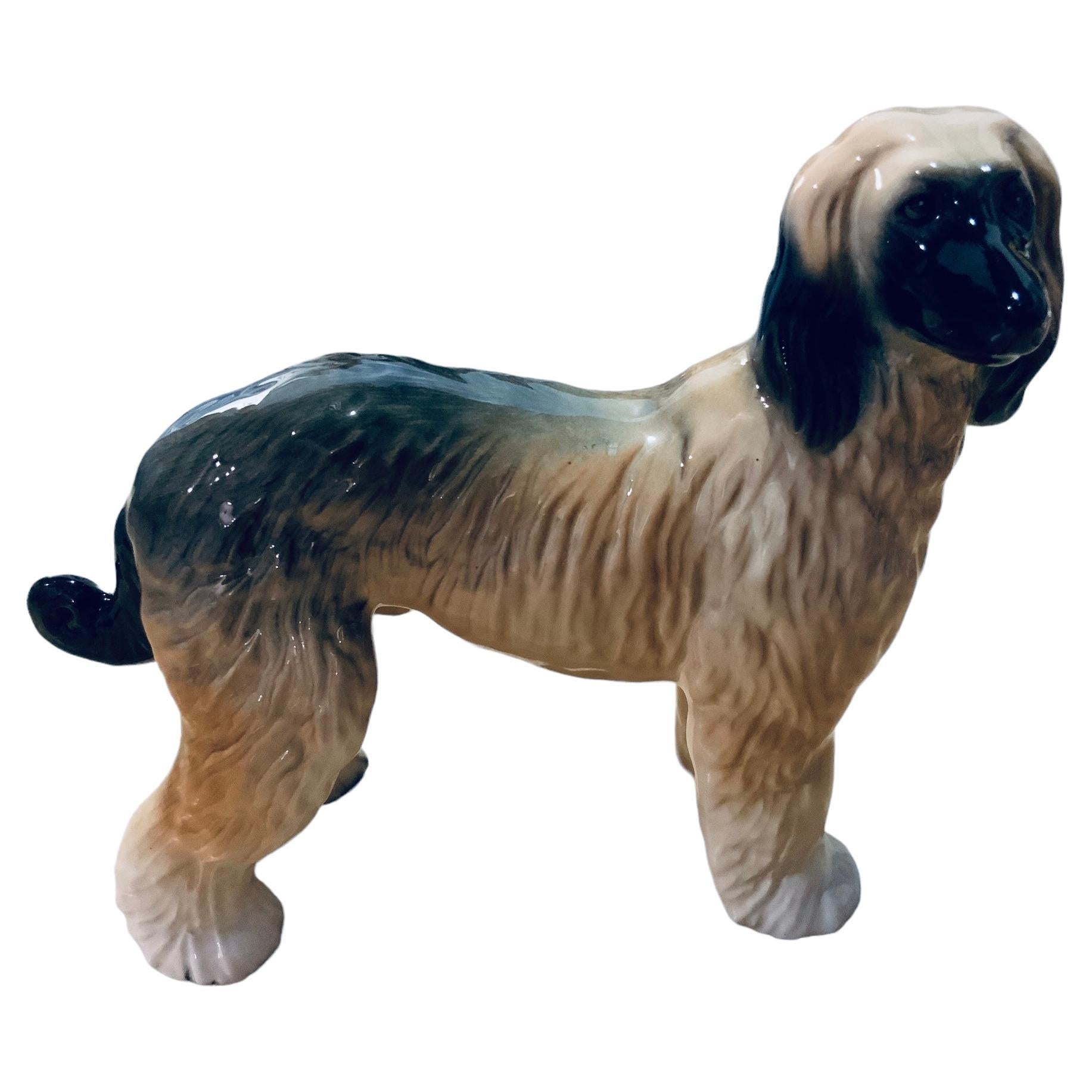 This is an English ceramic figurine of a dog. It depicts a very well done hand painted white, brown and black Afghan Hound dog. He is standing up well groomed and very proud of himself. 