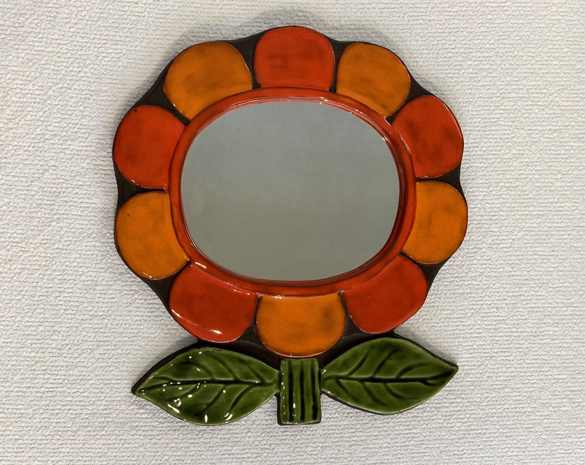 Ceramic mirror, figuring a 10 petals flower and 2 leaves, enameled in bright orange, red and green.
Mithé Espelt, -
Lunel (South of France) 1970
 Green felt at the back of the mirror in very good condition.

This poetic work of art demonstrates