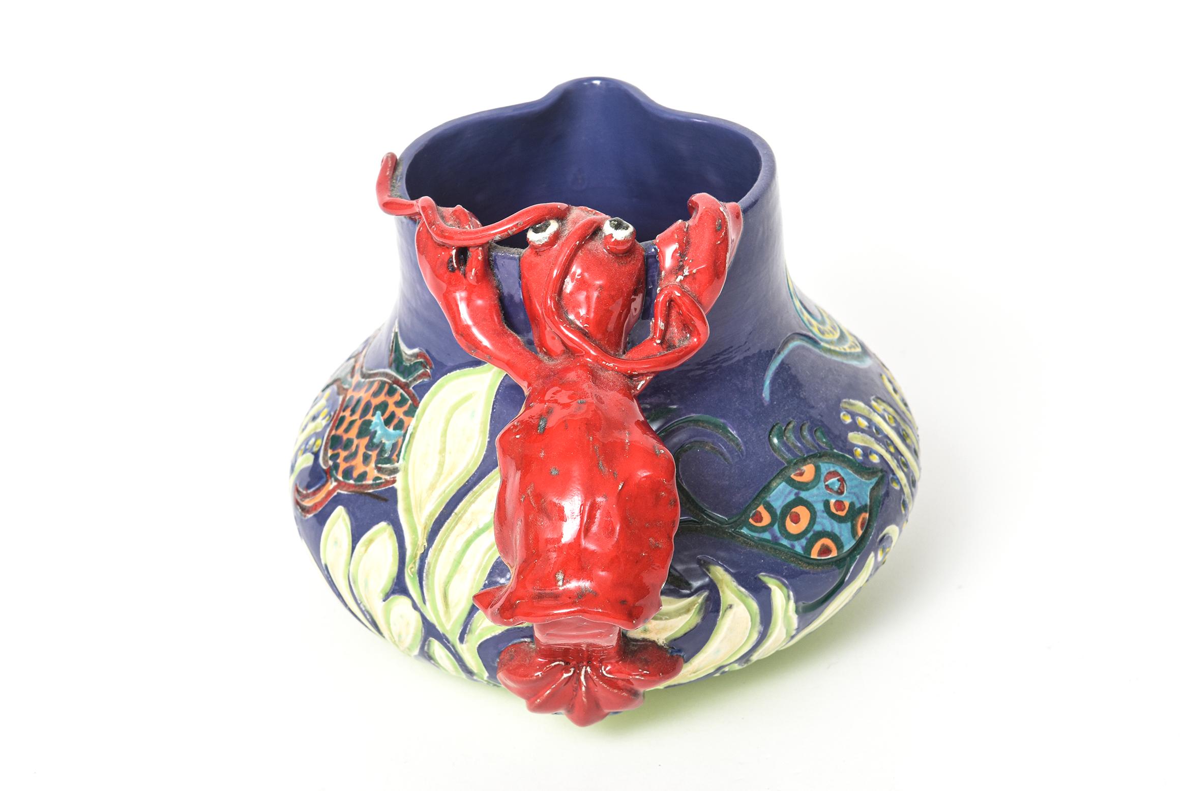 Unique handmade folk art pottery featuring a sealife design with fish swimming though a flowing underwater forest. The handle of the pitcher is a red lobster. The piece is signed but the signature is not legible. It is dated 1997 and number 011.