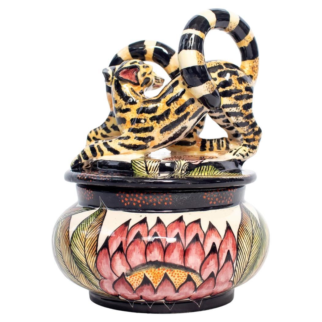 The Genet Cat jewelry box by Senzo Duma Ceramics, sculpted by Thabiso and hand-painted by Nqobile in 2023, measures 6 inches high, 5 inches in length, and 5 inches in width. The genet cat, found in African habitats, symbolizes grace, agility, and