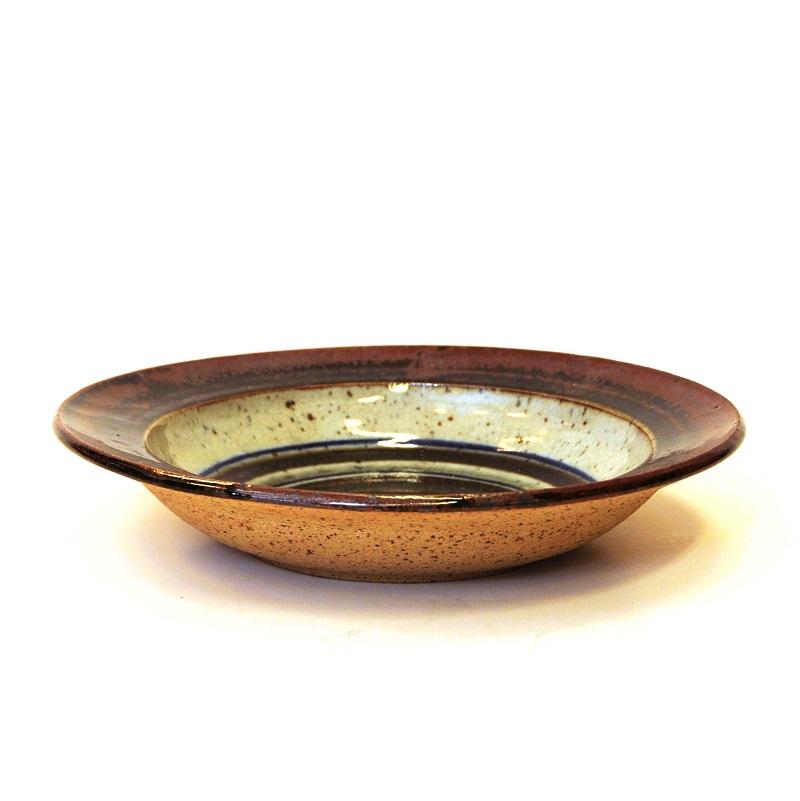 Lovely earth colored pottery dish by Helle Allpass, Denmark 1970s.
This lovely bowl or dish has a rustic glazed surface and a delicate shape. The plate has striped beige and brown inner decor lines with a cobolt blue color all around. Good vintage