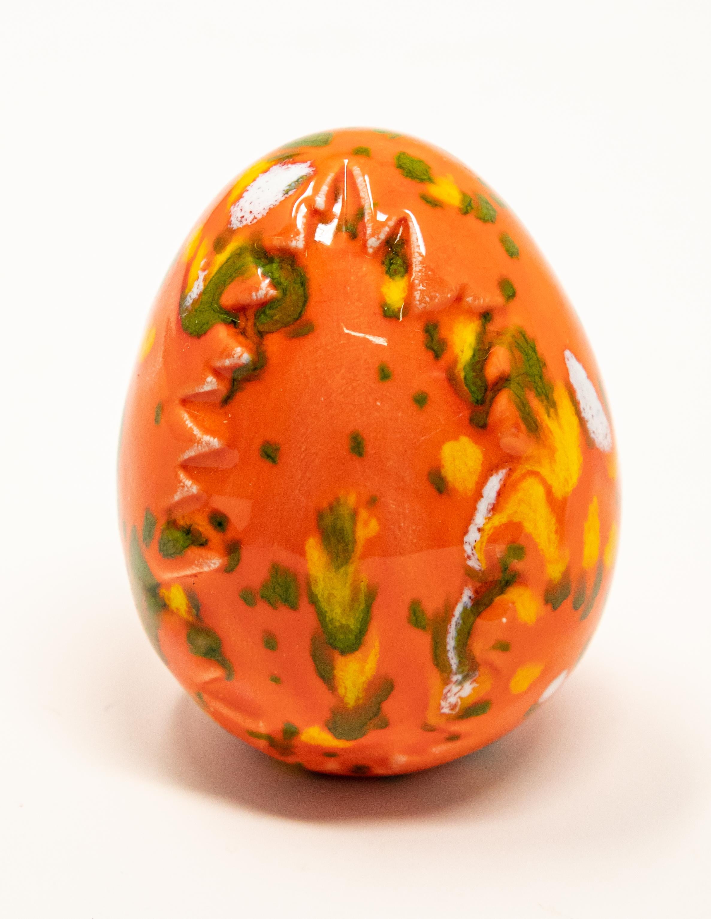 Offering this pair of ceramic glazed eggs. One is bright orange with green and yellow, and has a tree stamped in it. The other is cream and white, with accents of orange and yellow. Also has striped and geometric patterns.