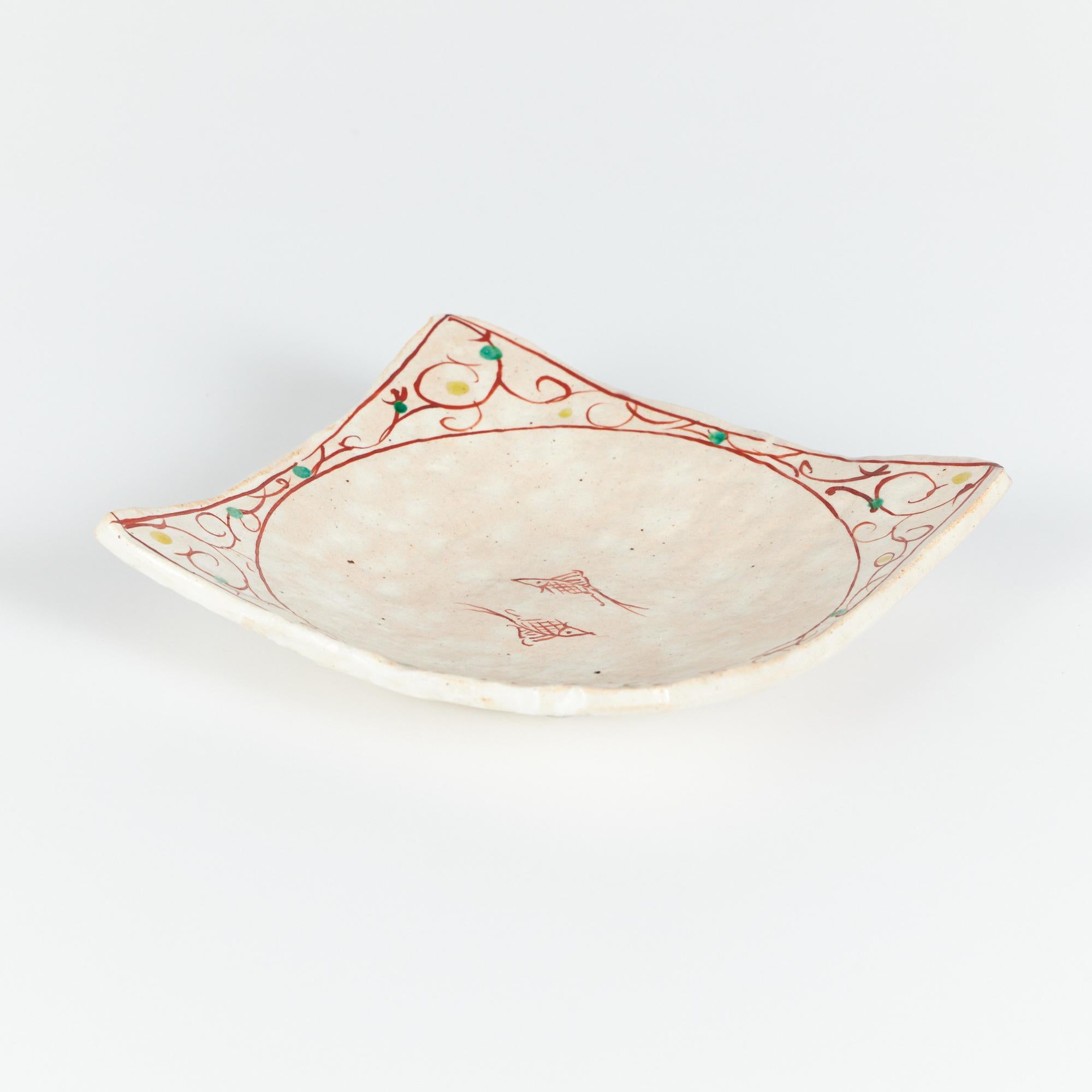 Der Keramikteller hat eine quadratische Form mit umgedrehten Ecken. Der Teller ist in einem weichen cremefarbenen und beigen Farbton glasiert, der durchgehend gesprenkelt ist. Das Stück ist mit zwei handgemalten roten Fischen in der Mitte des