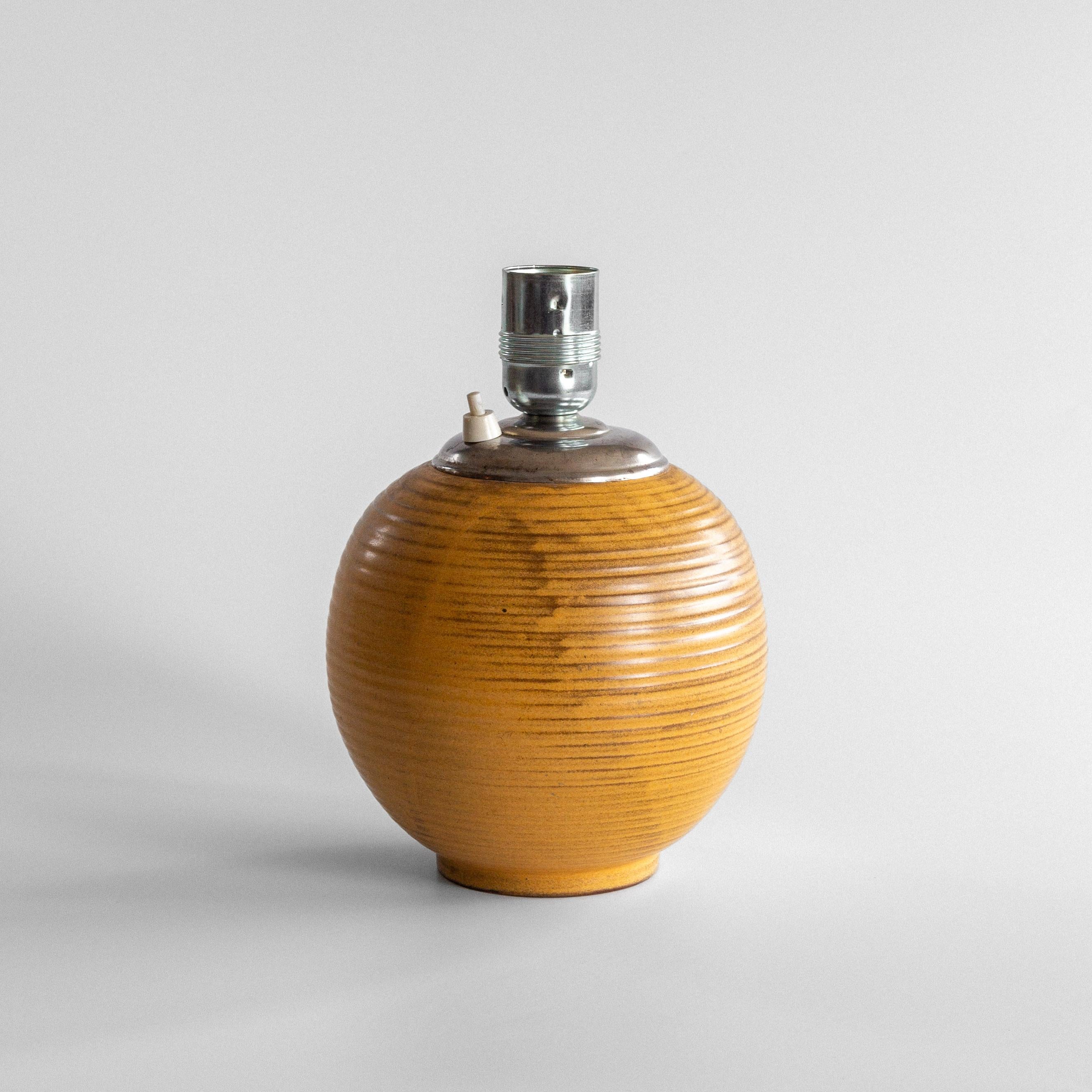 This earthenware table lamp, crafted by Upsala Ekeby, Sweden, in the 1930s/40s, features a glaze in warm tones between orange and beige with brown accents. The horizontal lines create a ribbed, textured surface, enhancing its earthy feel and