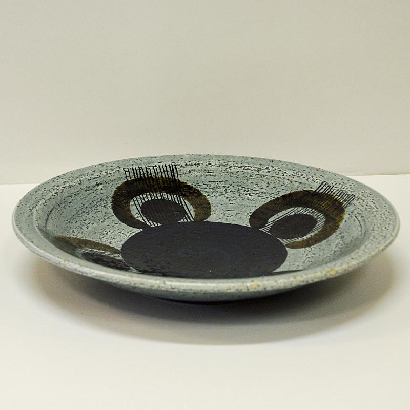 Highly collectible Swedish Mid-Century modern ceramic dish or bowl  of the Kurbits series designed by Olle Alberius for Rörstrand, Sweden 1960s. Handpainted chamotte clay on a grey base and dark blue bottomdecor with circles of plum colored sections