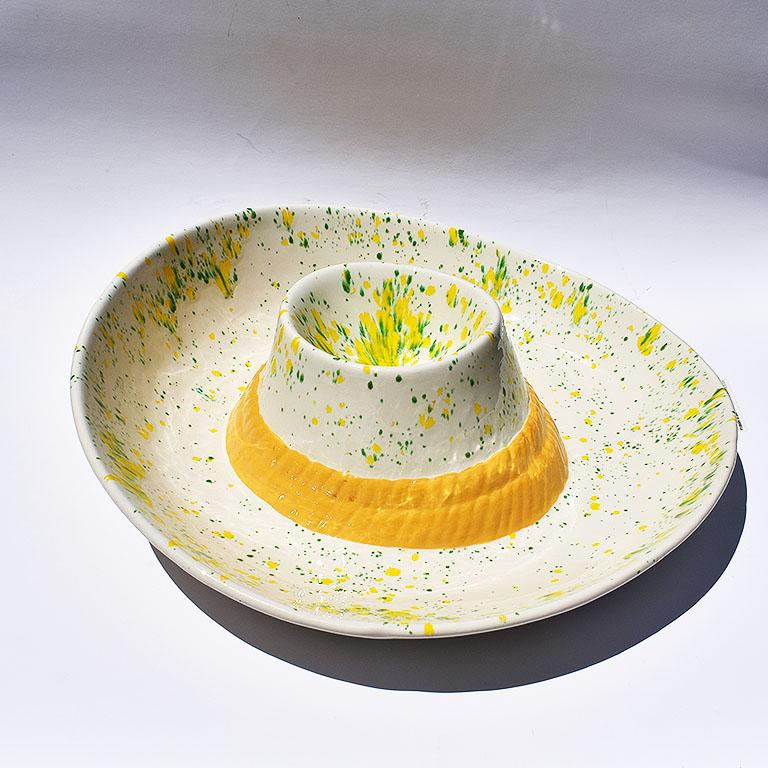 Ceramic hat themed platter with ribbon. A beautiful accent to any soirée. Round in form, this dish is shaped like a sun hat or cowboy hat. It reminds of a 1970s hat. Envision a portrait of Slim Aarons, with women dressed in brightly colored