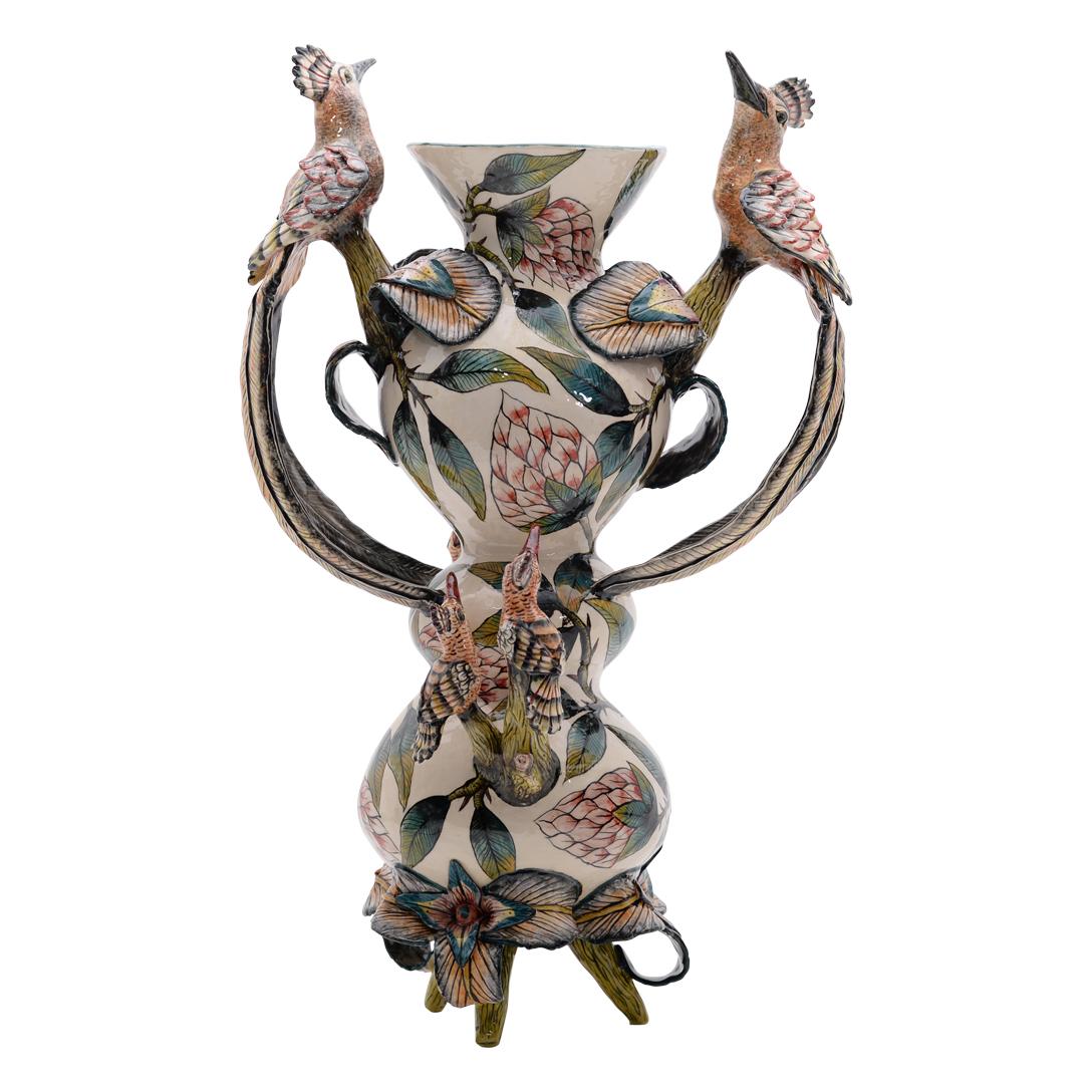 The Hoopoes and Proteas vase is a stunning example of South African ceramic artistry, crafted by the skilled hands of Lindy and Victor at Zimele Ceramics. This exquisite piece, standing 23 cm tall, 15 cm in length, and 12 cm in width, showcases a