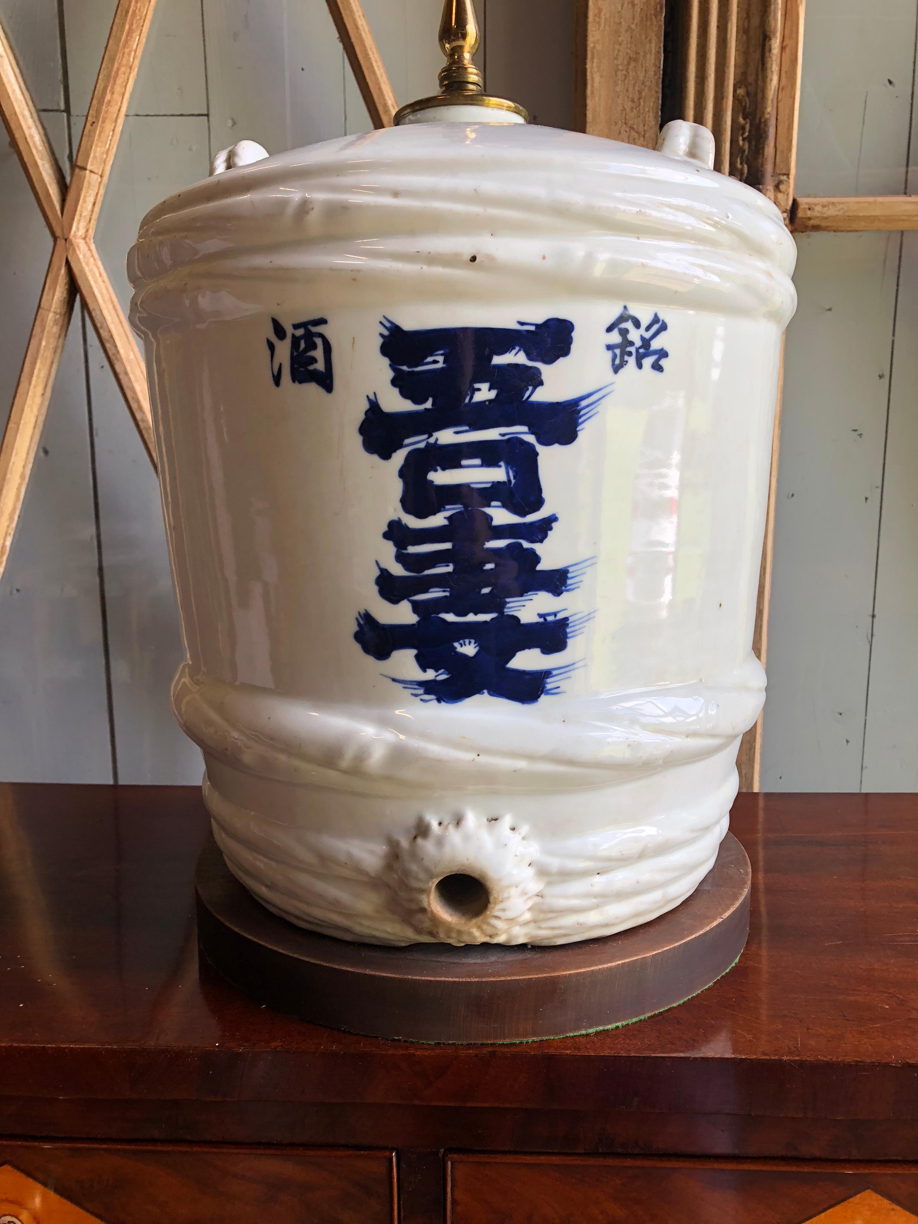 A large antique Japanese Sake Barrel in white ceramic with cobalt blue lettering, circa 1900, now mounted as a lamp on a wood base. 
 
