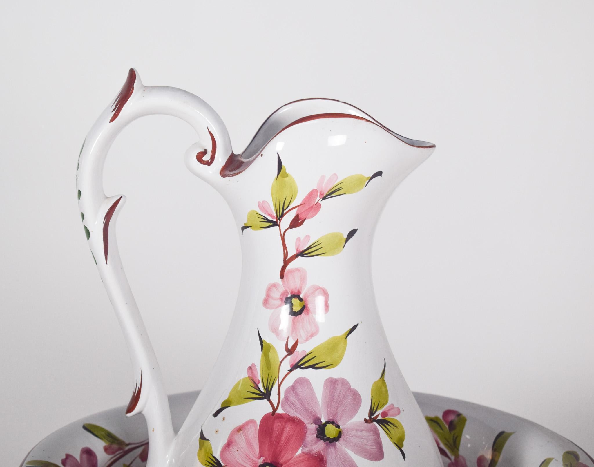 Keramische Kanne und Becken. Polychrome Dekoration mit Blumen. Die Kanne hat ein elegantes Design mit weichen Rundungen und einem leicht gewellten Ausguss. Der mit blattförmigen Details verzierte Griff unterstreicht die Zartheit des Stücks. Beide
