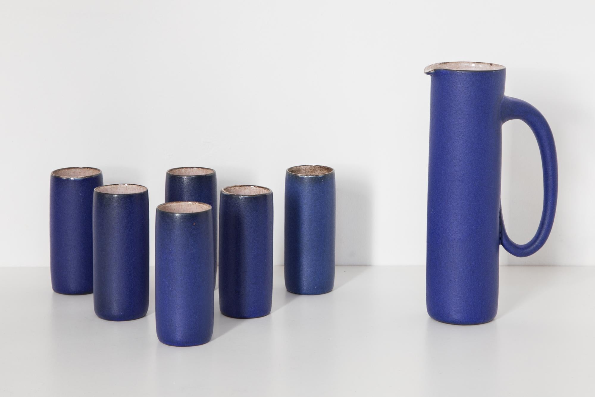 The tall six mugs and pitcher has an elegant Minimalist styling a narrow cylindrical neck and a narrow foot ring. The pitcher and mugs are glazed in a rich cobalt blue color with a matte finish. Perfect condition. Measures: Mugs 5 W x 13.5 H x 5 D