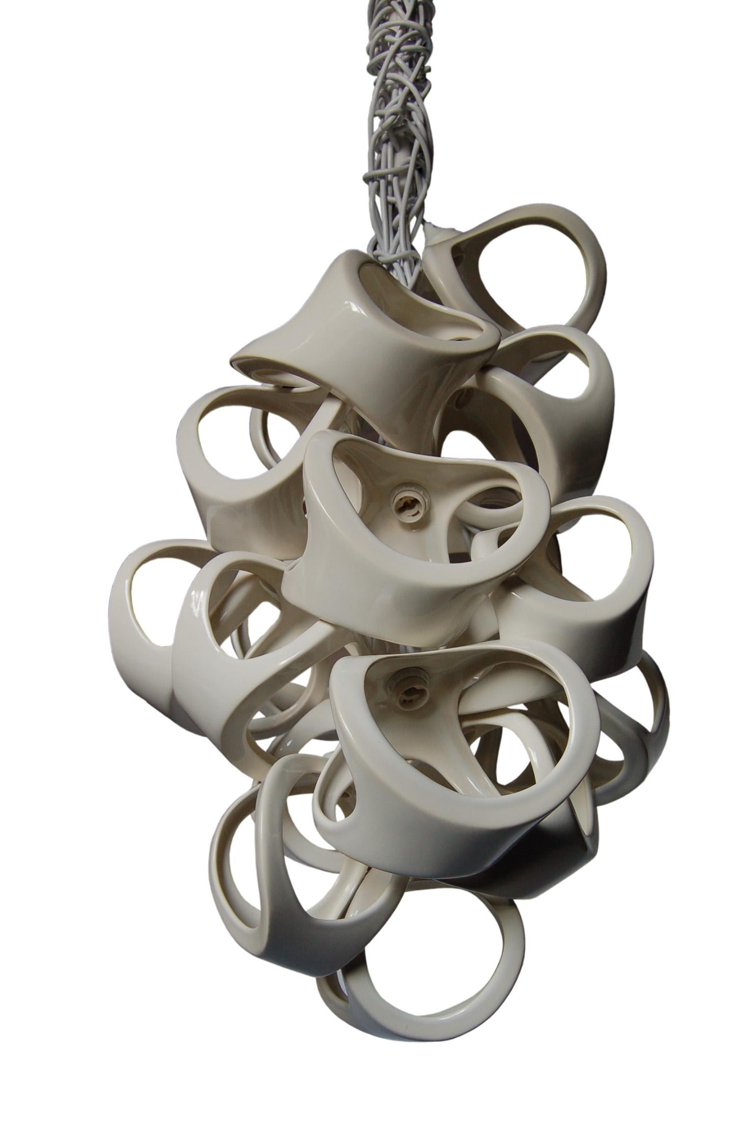 An organic grouping of 18 slip cast ceramic shades. The bone like forms nest together to form a sculptural fixture with dramatic shadows. White knotted cords accentuate the organic nature of the Ceramic Lamp series. Overall length of piece can be