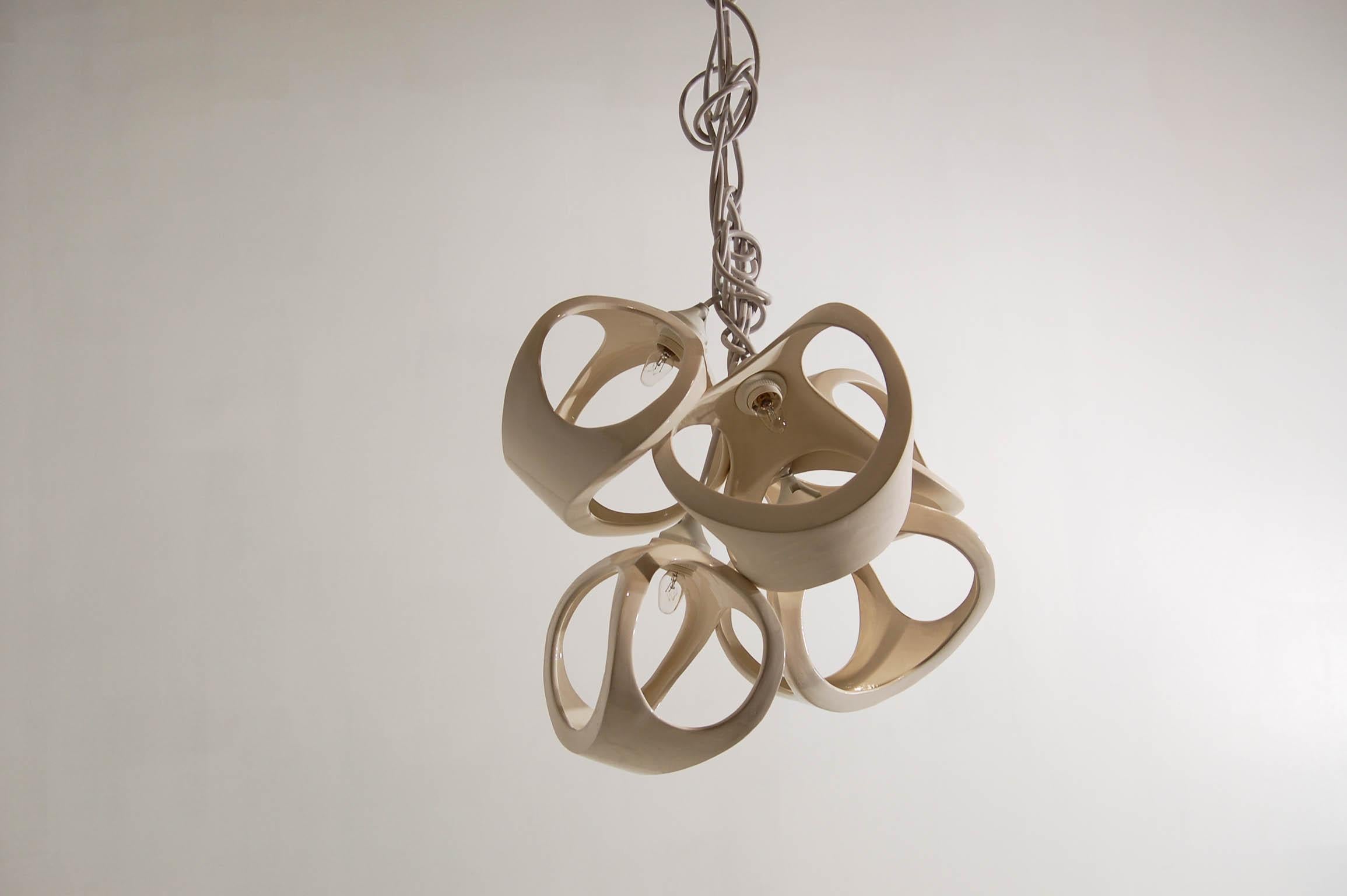A compactly clustered ceramic lamp chandelier of 5 overlapping slip cast ceramic shades. The bone like forms nest together to form a sculptural fixture with dramatic shadows and soft light. White knotted cords accentuate the organic nature of the