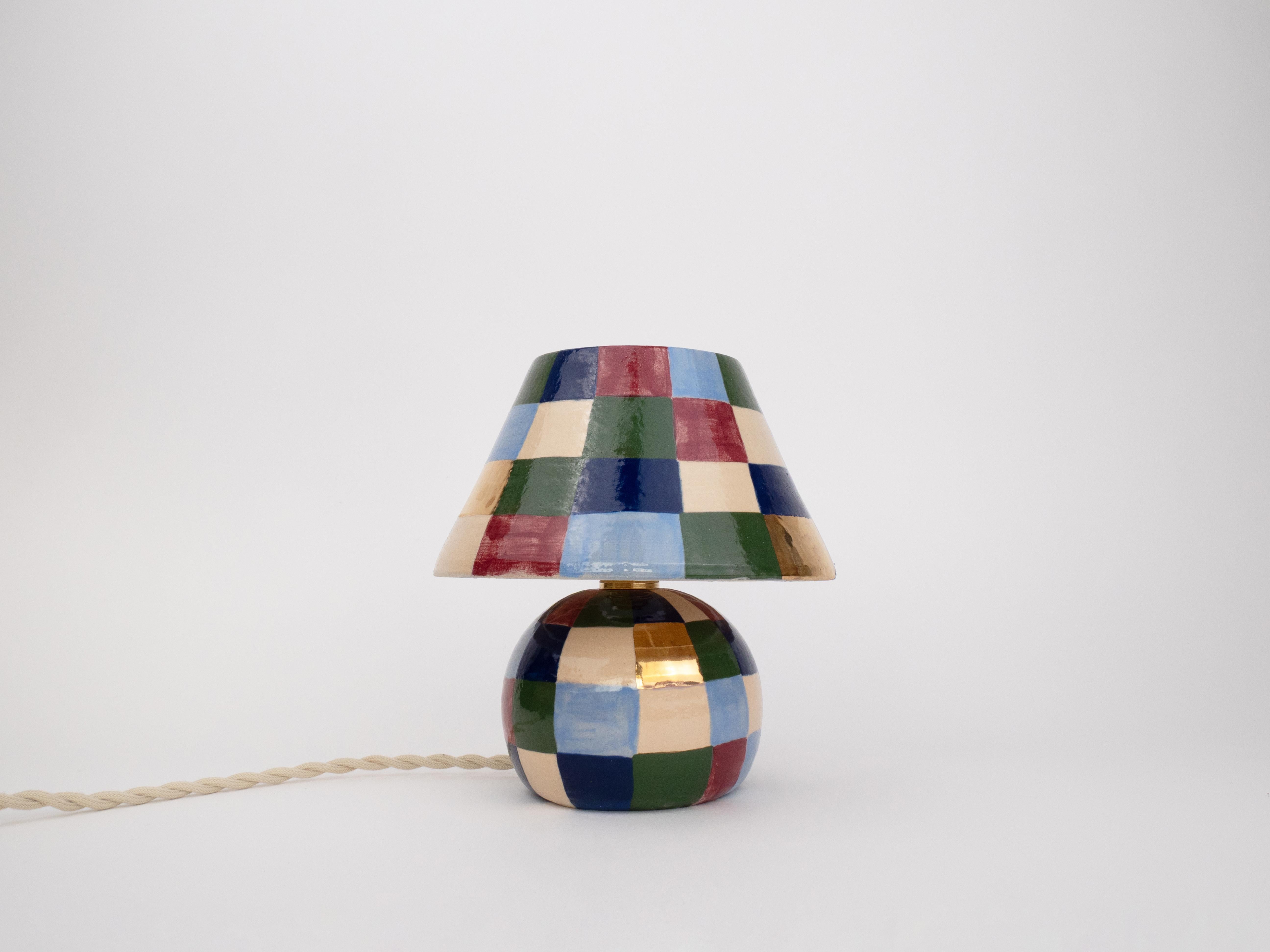 Add a touch of charm and elegance with this handcrafted patchwork table lamp. It features a vibrant mix of hand-painted squares and luxurious 24k gold detailing. With its glossy finish and artisanal design, this statement piece will bring warmth,