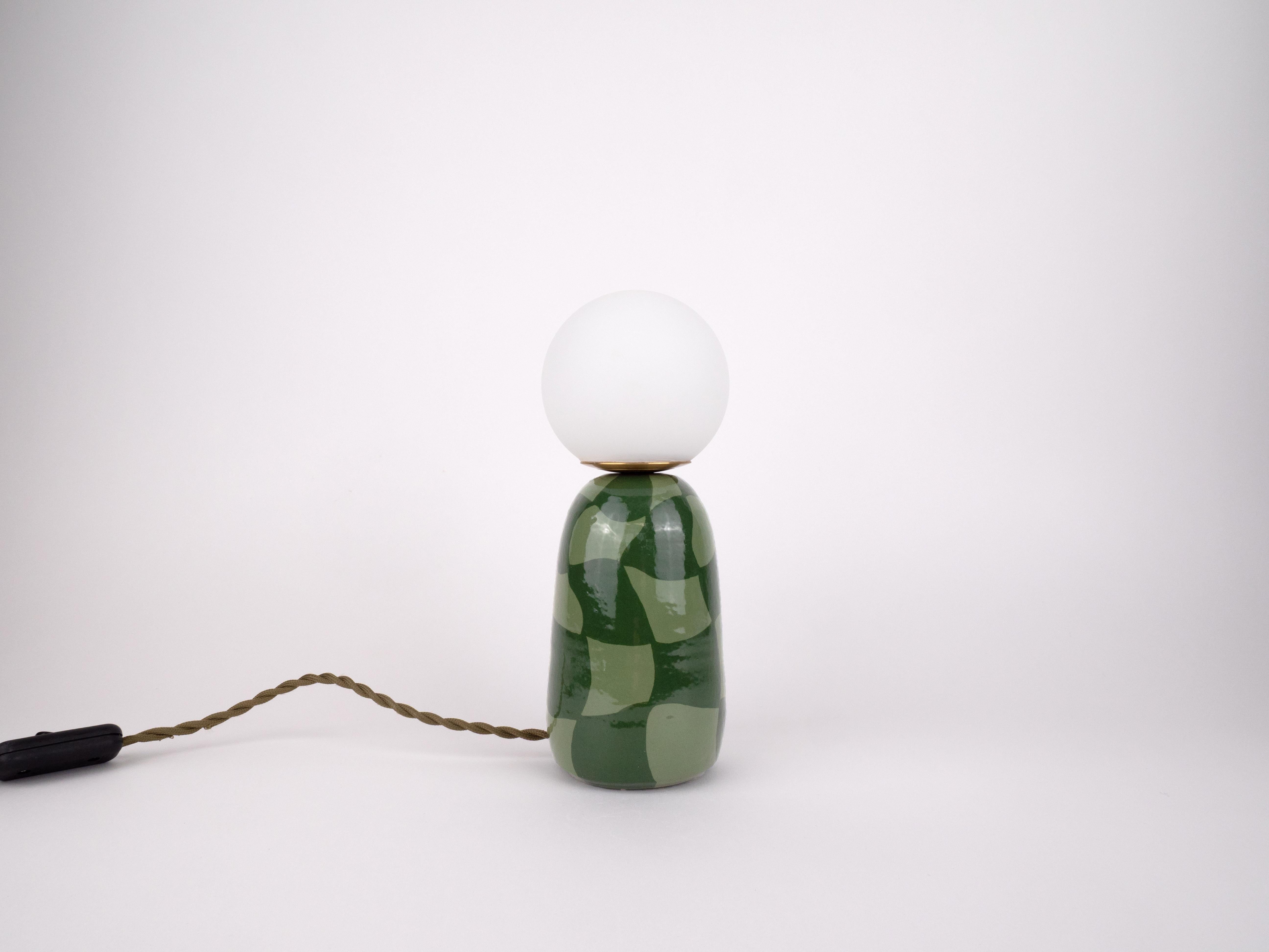 À la fois ludique et moderne, cette lampe en céramique fabriquée à la main associe une base à carreaux verts bicolores à une ampoule globe givrée pour une lueur confortable. Sa finition brillante et son design organique en font la petite pièce