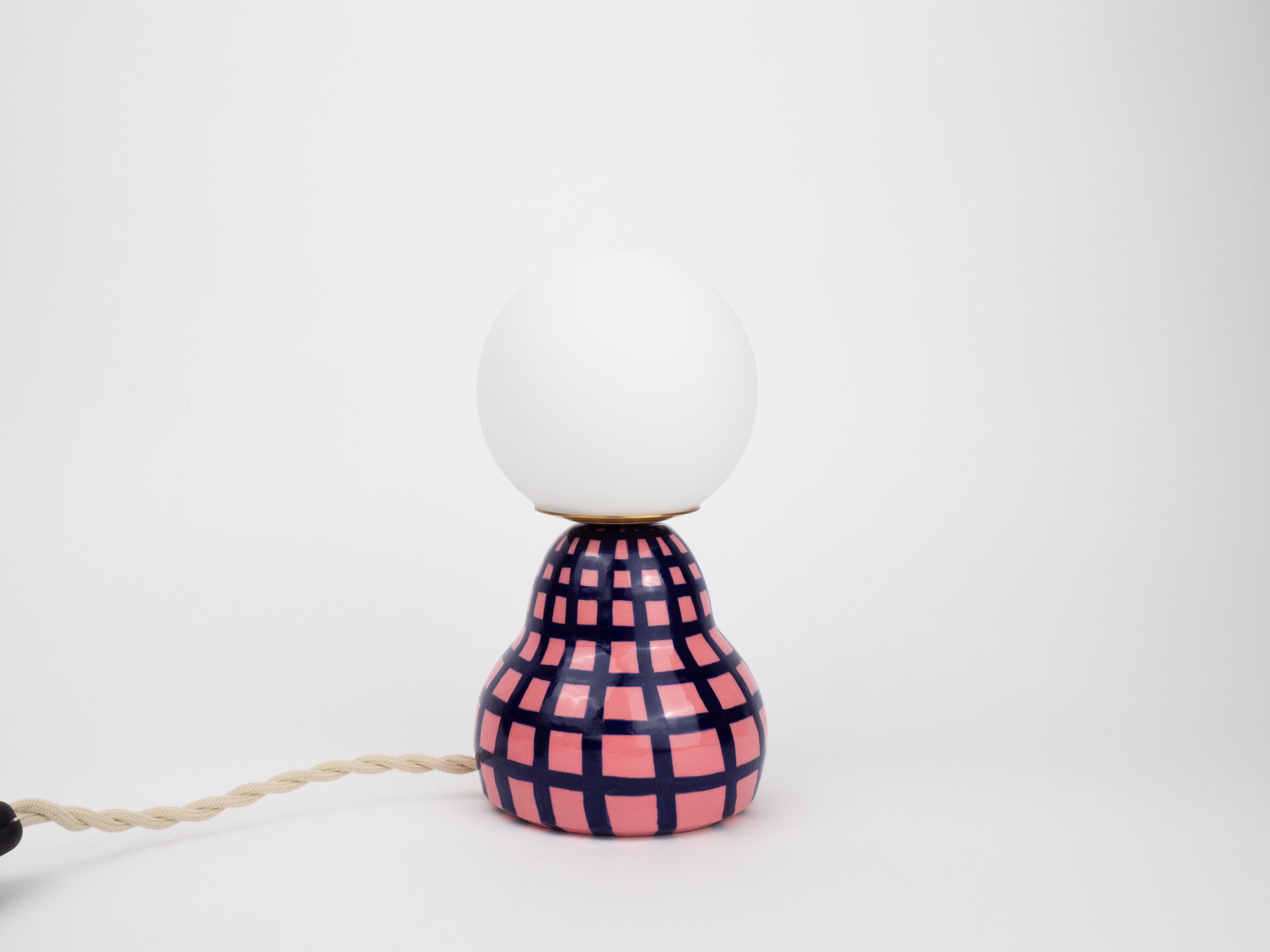 Divertida y única, esta lámpara de cerámica hecha a mano combina una base rosa y azul intenso con una bombilla globo esmerilada para un resplandor acogedor. Su acabado brillante y su alegre diseño la convierten en la pieza perfecta para cualquier
