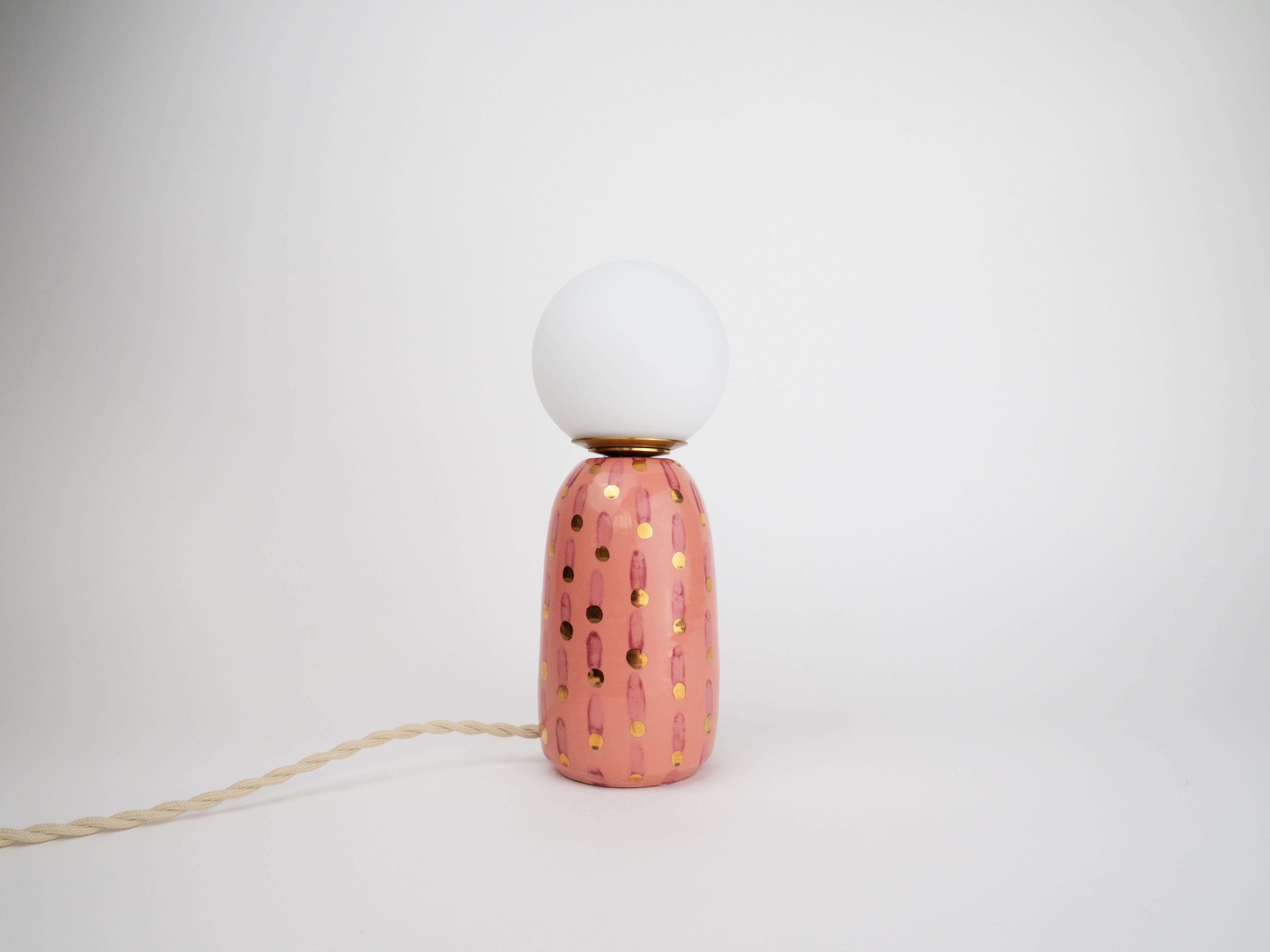 Cette lampe en céramique fabriquée à la main associe une base rose à une ampoule globe givrée pour une lueur chaleureuse. Son design ludique, sa finition brillante et ses luxueux détails en or 24k en font la petite pièce d'apparat parfaite pour tout
