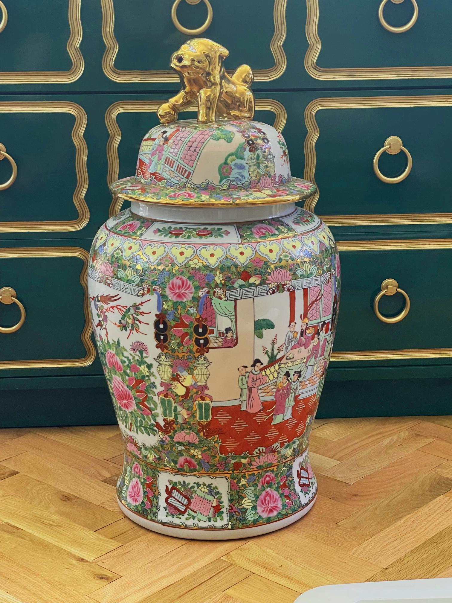 Ce grand vase ou urne en céramique présente un corps et un couvercle peints à la main en chinoiserie, représentant des scènes orientales ainsi que des oiseaux et de la flore. Le couvercle bombé est orné d'un foo dog doré en guise de poignée. La