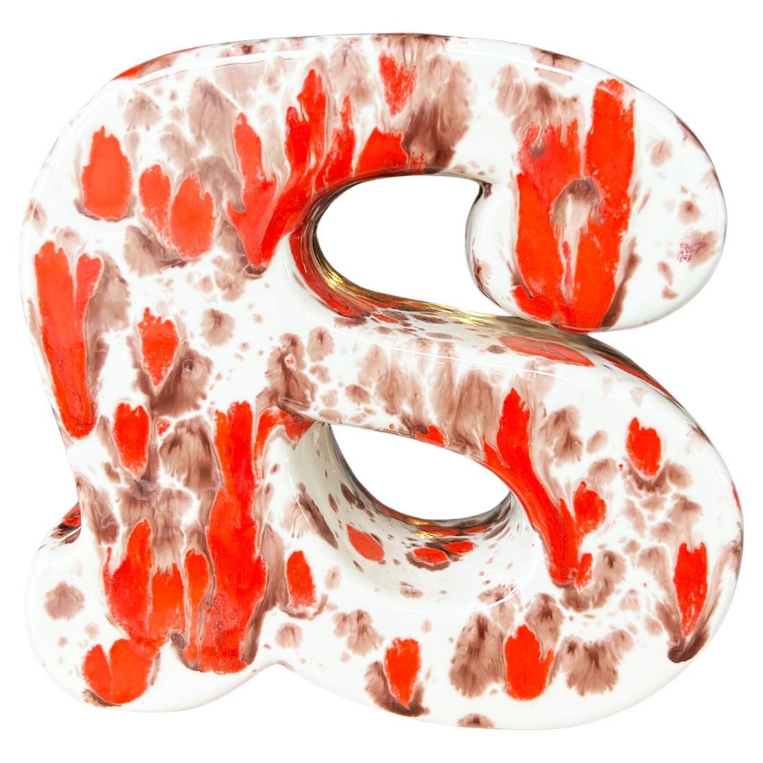 A ceramic lowercase letter A bookend. This piece was created in 1981 and painted in an orange, red, and brown splatter pattern. 

Dimensions:
6